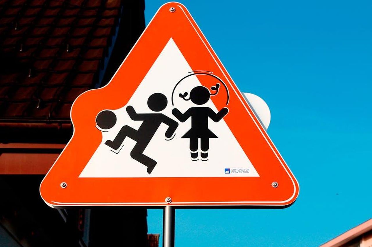 Il_piccolo_Michelino_rischi_di_essere_investito_con_lauto_da_Odile_negli_episodi_precedenti_M3ebQZsf5z - Confidenze24 Source: Roly Vasquez - pexels - Triangular road sign depicting children playing, emphasizing safety against a bright blue sky.