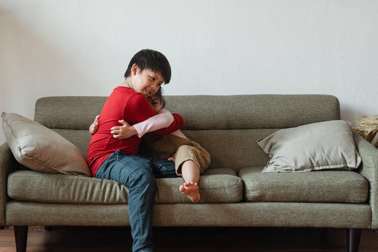 Il_rapporto_di_Emma_con_la_madre_e_la_famiglia_allargata_yuzdYTLdhC - Confidenze24 Source: Ketut Subiyanto - pexels - Two children sharing a heartfelt embrace on a cozy living room sofa, expressing love and joy.