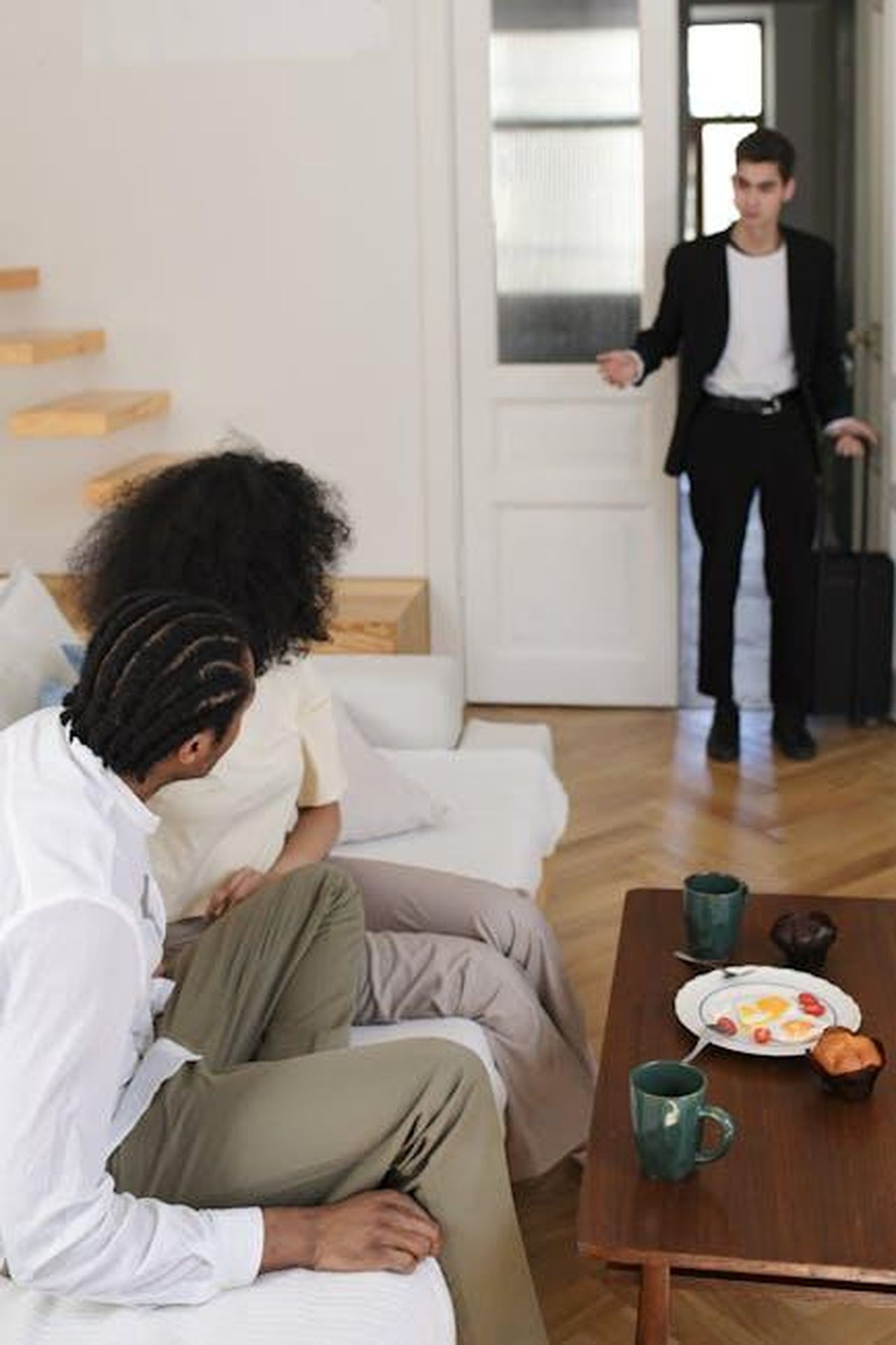 Il_ritorno_inaspettato_c0HhsOWMfi - Confidenze24 Source: Ron Lach - pexels - Young man returns home surprising a couple seated on the sofa, sparking intrigue and emotion.