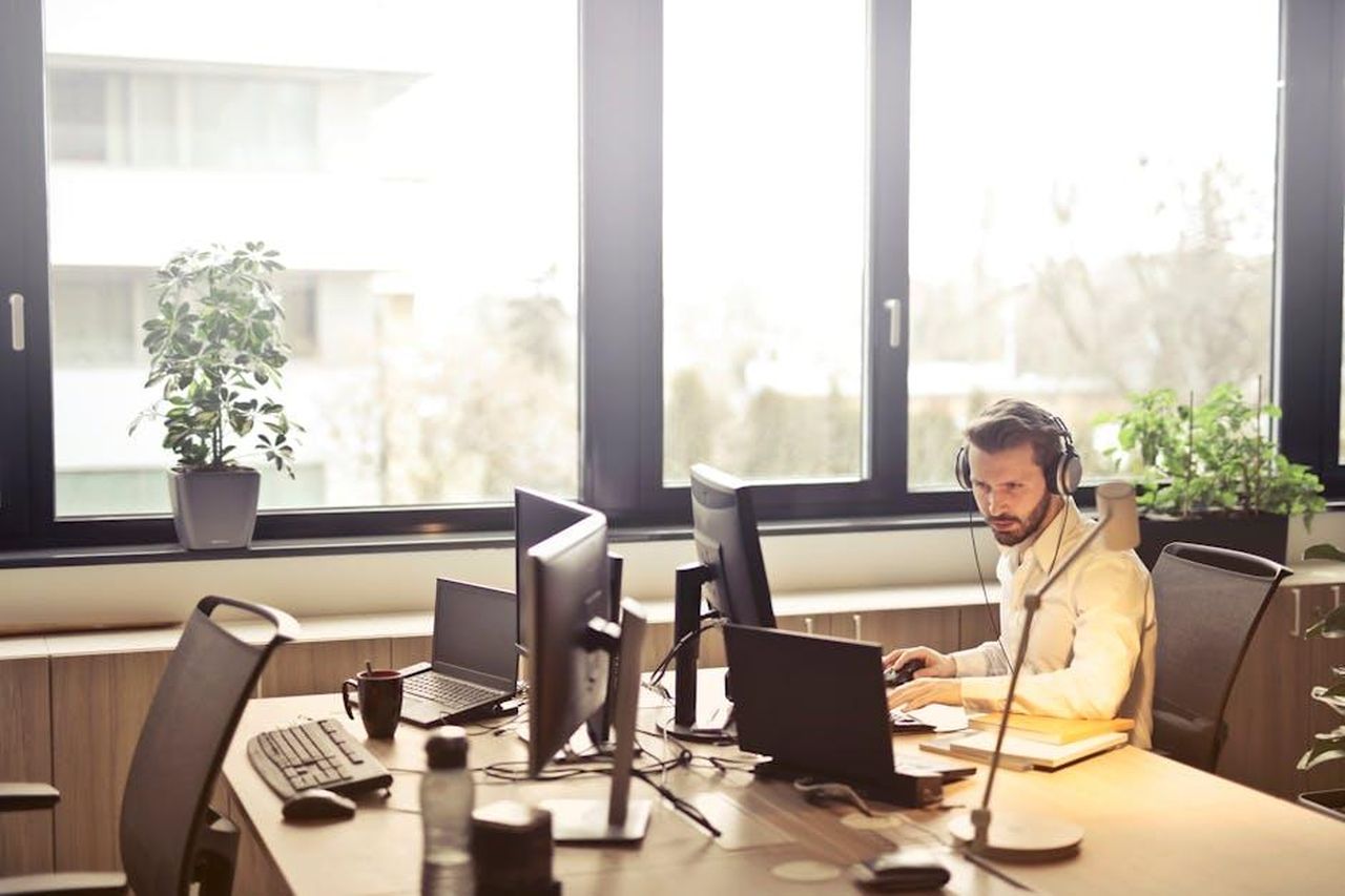 Il_supporto_dei_clienti_per_il_marchio_As_Ever_EF17mSOj7Q - Confidenze24 Source: Andrea Piacquadio - pexels - A businessman sits at a desk using multiple computers and a headset in a well-lit modern office.