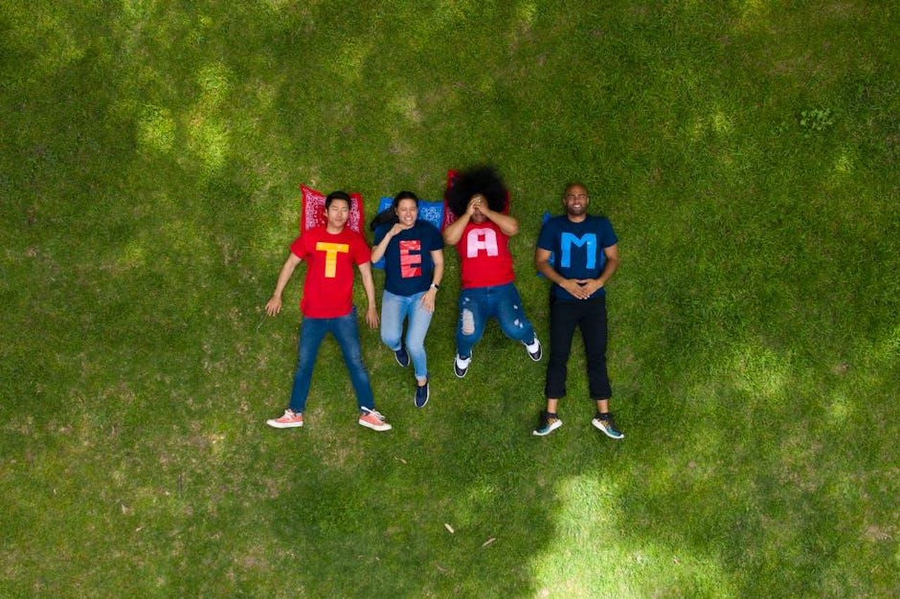 Il_supporto_di_Rachel_Maddow_NcEpI8QpMk - Confidenze24 Source: RDNE Stock project - pexels - Diverse group of adults lying on grass with TEAM shirts, symbolizing teamwork and togetherness.