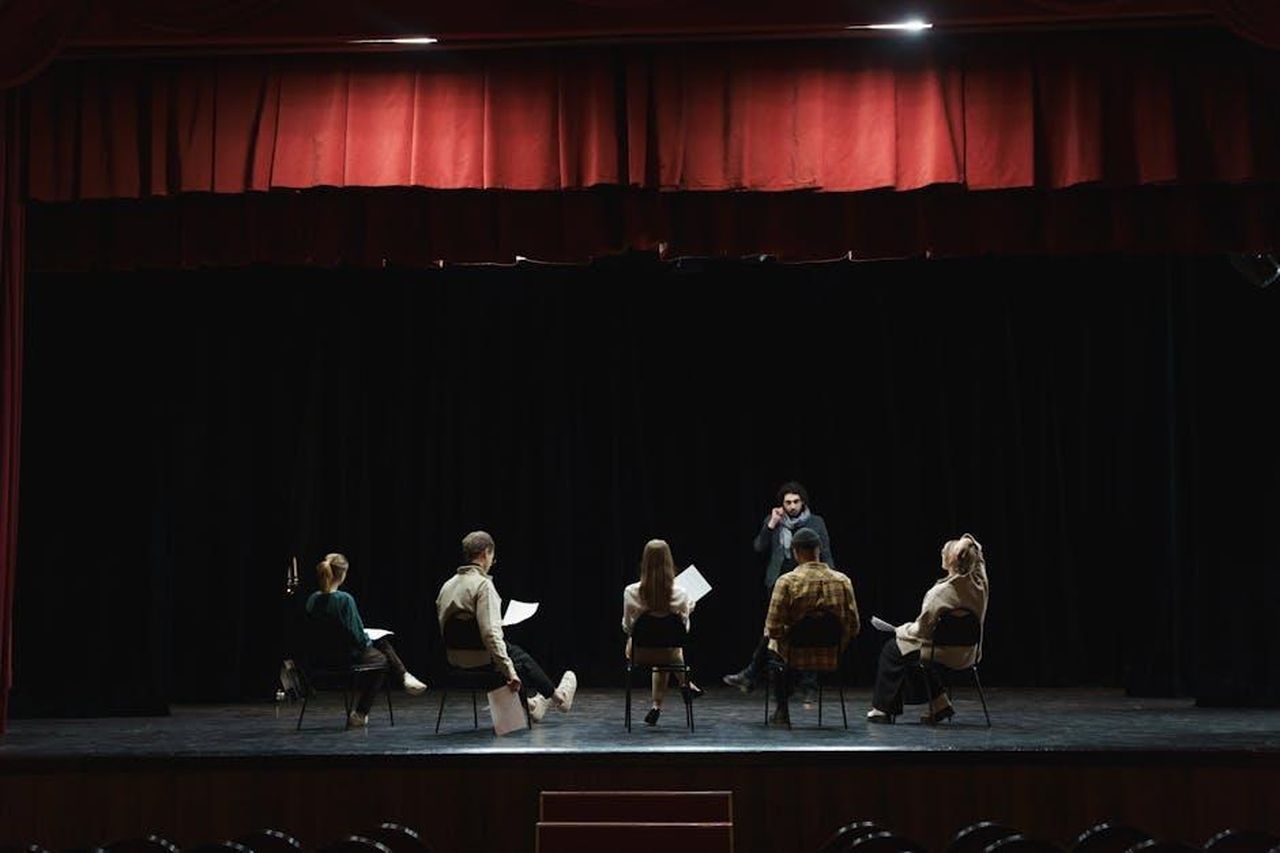 Il_via_vai_in_studio_1Q9s7NdUWf - Confidenze24 Source: cottonbro studio - pexels - A group of actors rehearsing on a dimly lit stage in an auditorium, preparing for a theater performance.