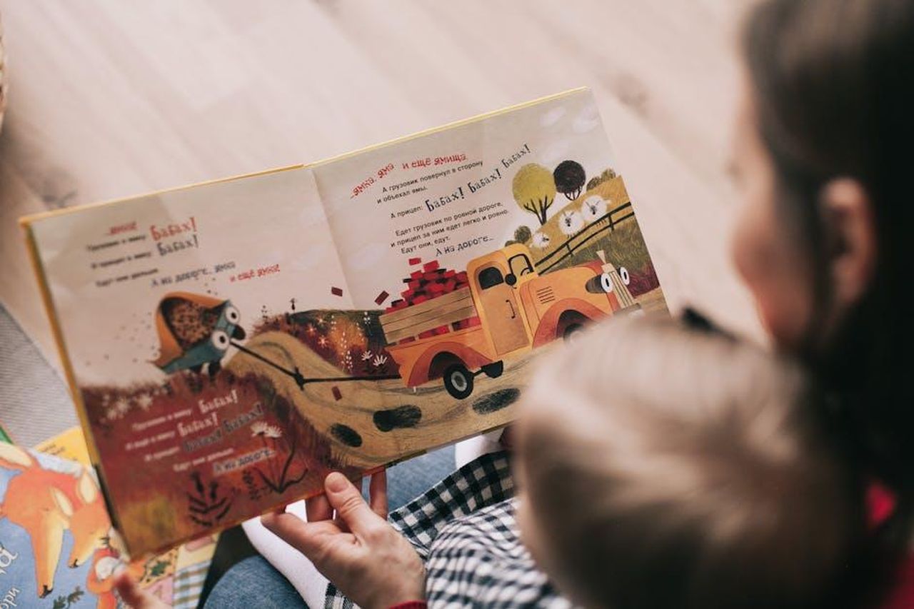 Il_viaggio_di_Yesim_e_la_richiesta_di_Oyku_DnsqOxQB3t - Confidenze24 Source: Lina Kivaka - pexels - A mother and toddler sharing a story from an illustrated children's book indoors.