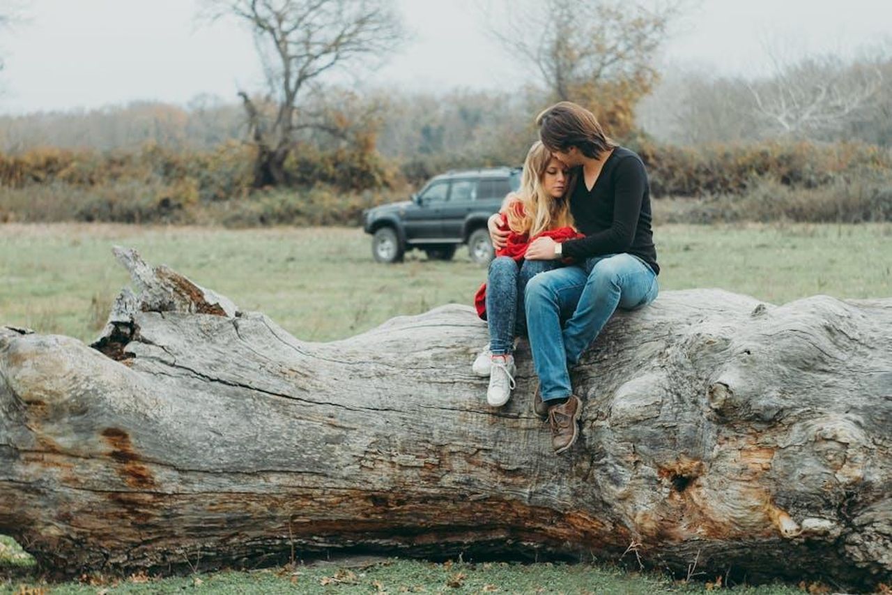 Ipotesi_trame_future_Guido_pu_essere_ancora_innamorato_di_Mariella_kDGvuvKasr - Confidenze24 Source: Anastasiya Lobanovskaya - pexels - A couple embraces tenderly on a large fallen tree, set against a serene natural landscape.
