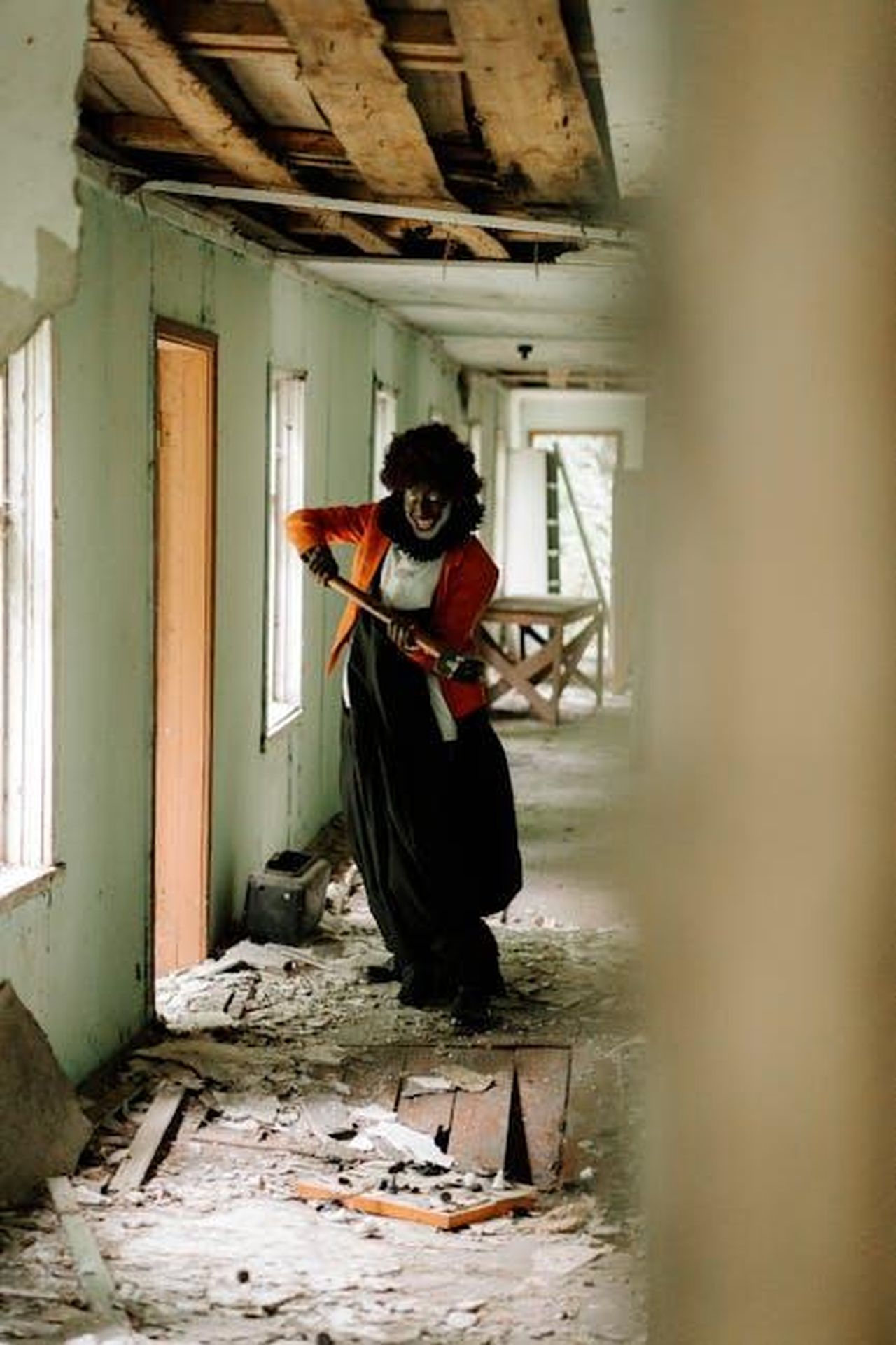 La_Finale_di_The_Chase_CXP5TzepPj - Confidenze24 Source: cottonbro studio - pexels - Eerie scene of a frightening clown in tattered costume holding a weapon in an abandoned hallway.