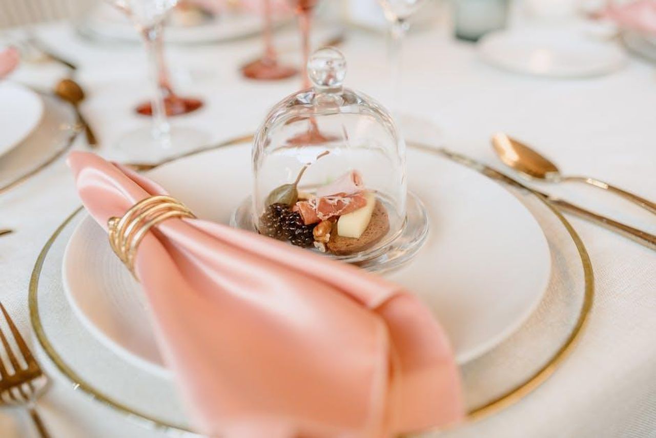 La_cena_di_San_Valentino_ItVNCd0LR9 - Confidenze24 Source: Bruno Cervera - pexels - Luxe table setting featuring a cheese and nut platter under glass with a pink napkin.