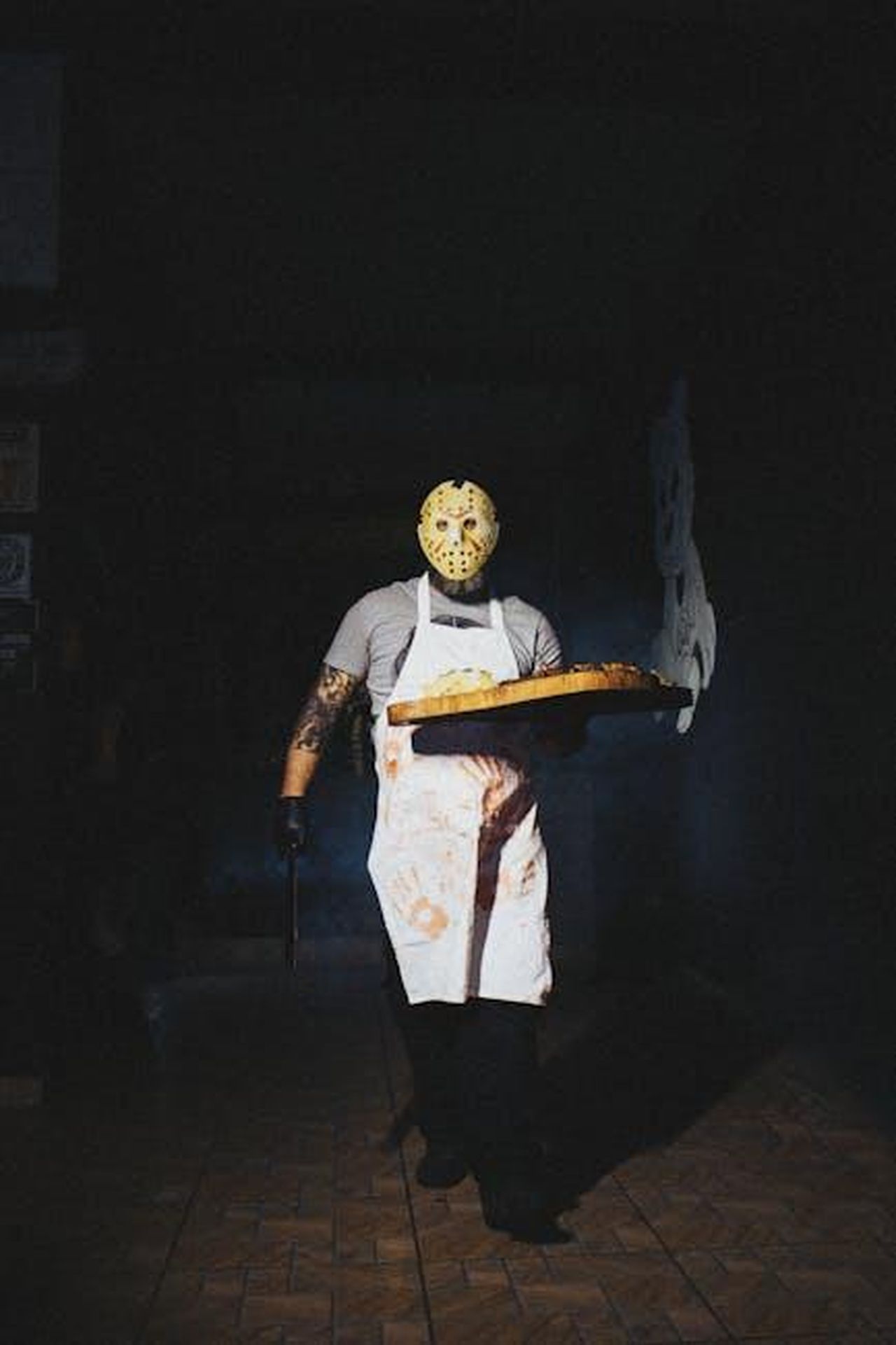 La_conclusione_della_partita_zJlMegz7y8 - Confidenze24 Source: Matheus Bertelli - pexels - A man in a horror mask and apron serves pizza in eerie lighting, creating a spooky feel.