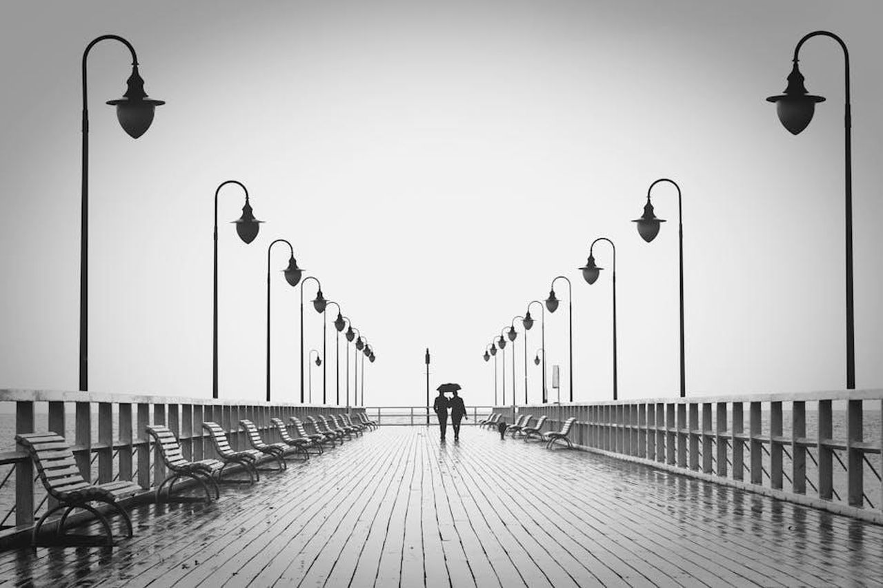 La_connessione_speciale_tra_Travis_e_Taylor_qpBihYy9hY - Confidenze24 Source: Pixabay - pexels - A couple holding umbrellas walks on a rainy boardwalk, embodying romance and tranquility.