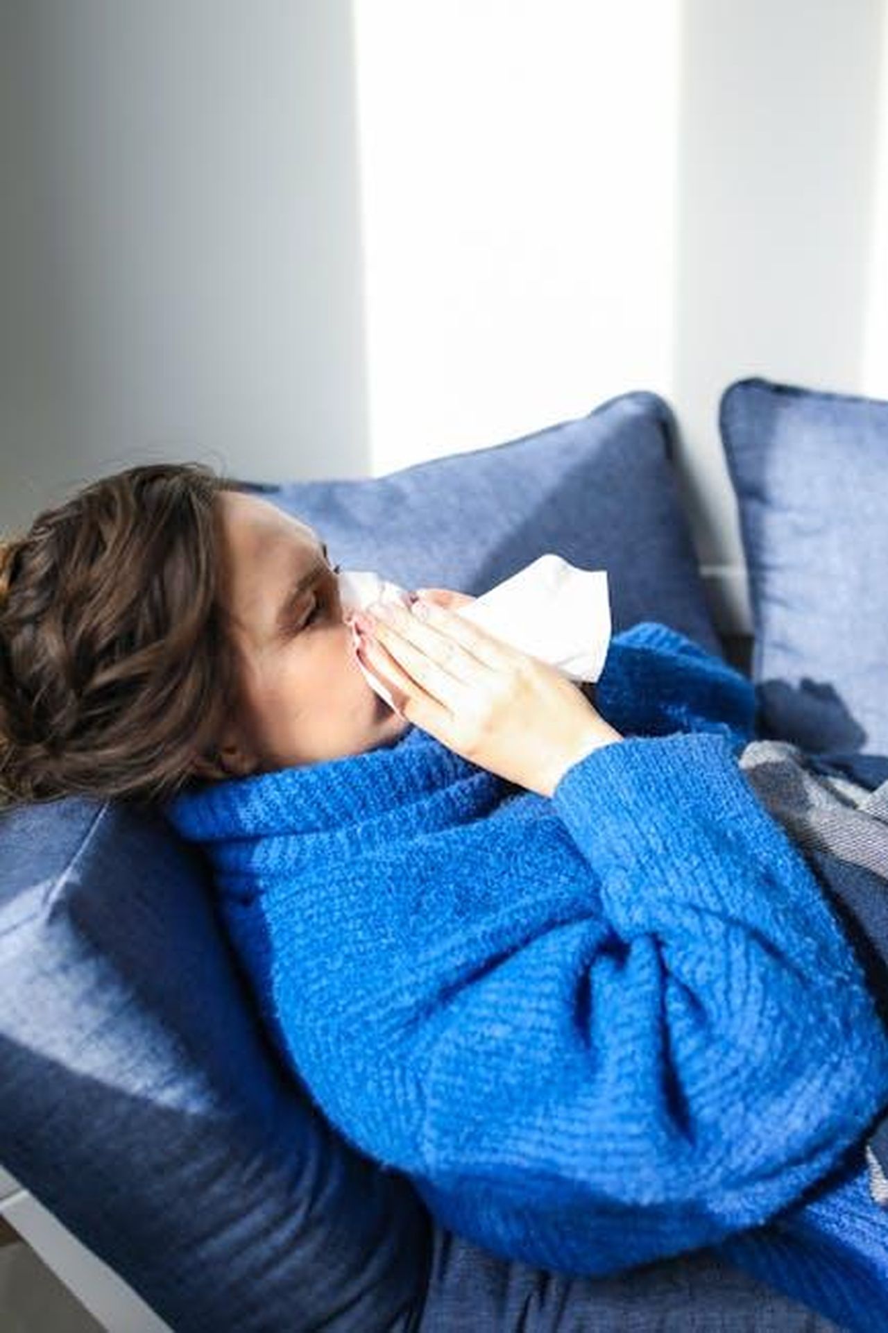 La_contagiosit_del_morbillo_xR1X21xcAi - Confidenze24 Source: Polina Tankilevitch - pexels - A woman in a blue sweater uses a tissue, lying indoors, suggesting illness or flu symptoms.