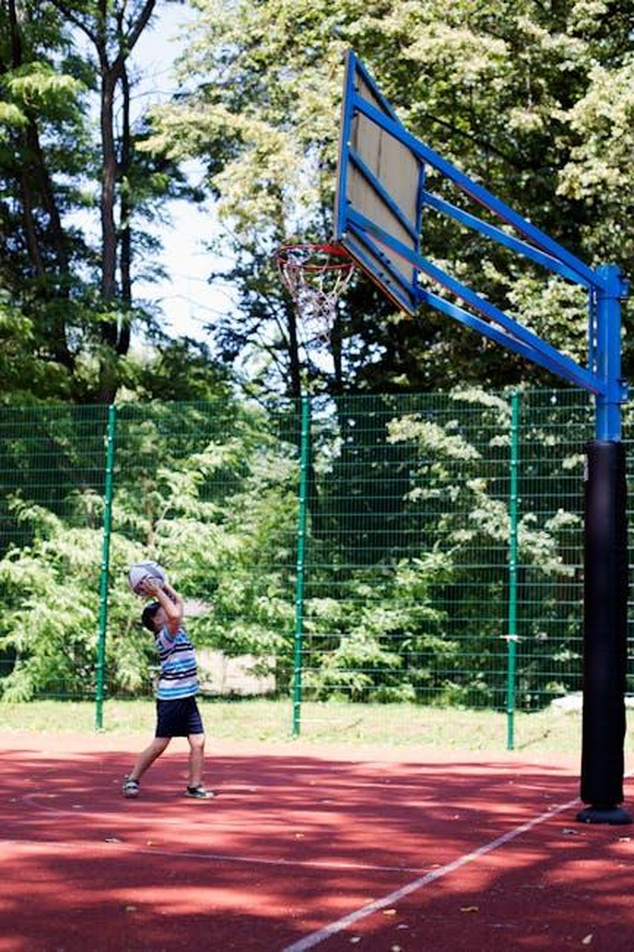 La_decisione_di_Rihanna_di_portare_i_bambini_in_aula_EkzaxBB10i - Confidenze24 Source: Mariana Kurnyk - pexels - A child playing basketball on an outdoor court surrounded by trees on a sunny day.