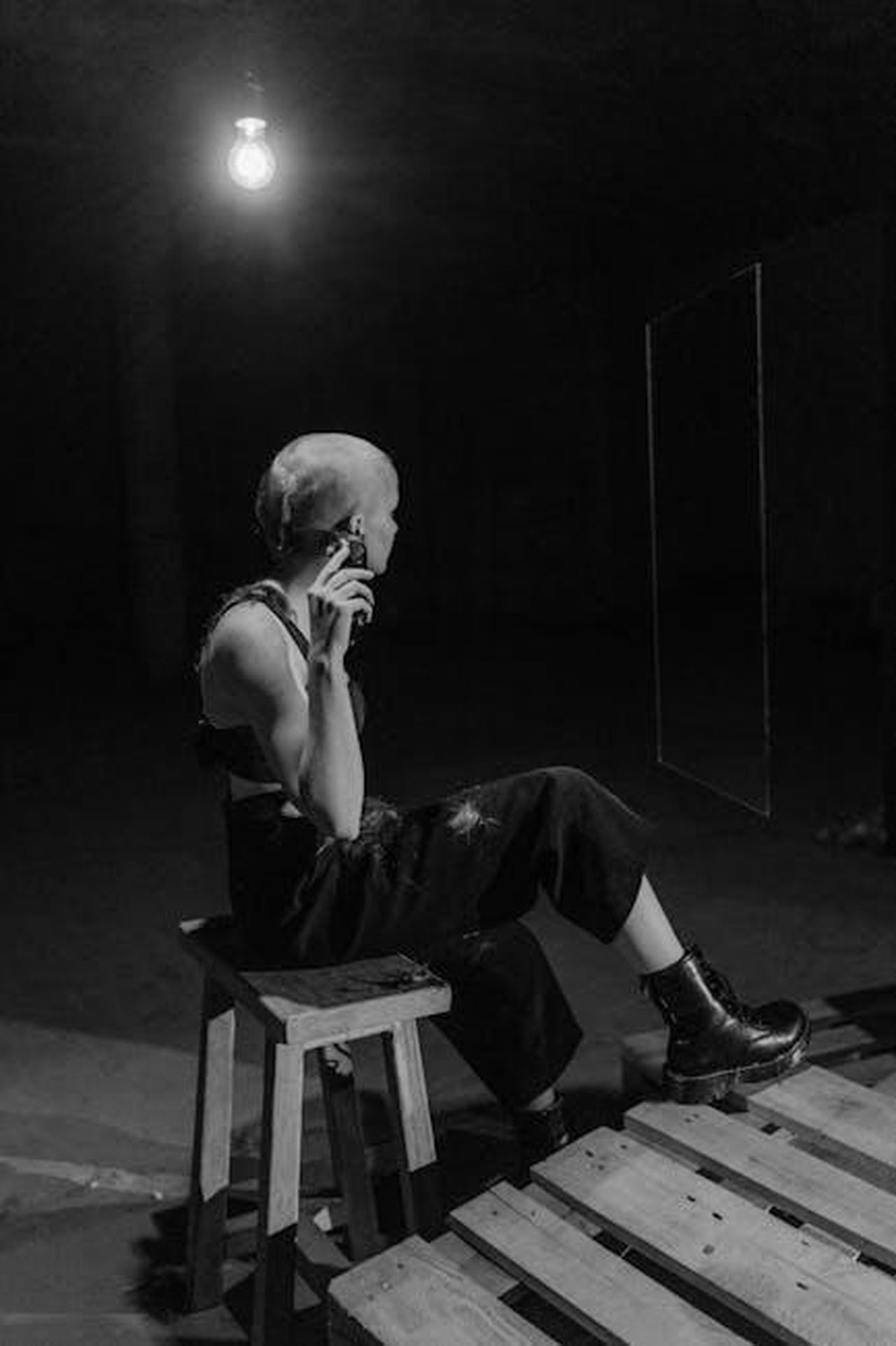 La_difficile_decisione_oWXaRtIIoe - Confidenze24 Source: Tima Miroshnichenko - pexels - A woman in dark attire shaving, seated dramatically under a bulb in a black and white portrait.