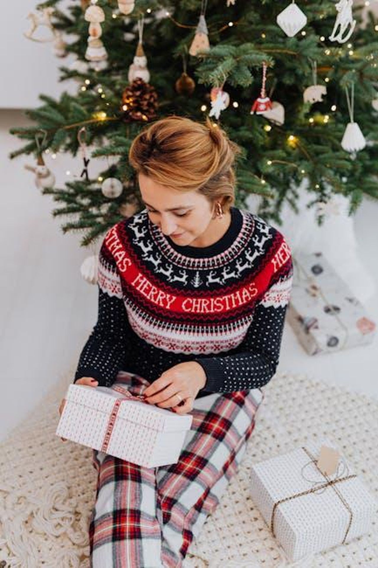La_felicit_di_Maria_e_la_delusione_di_Virtudes_SQgWWId5gN - Confidenze24 Source: Photo By: Kaboompics.com - pexels - Woman in a festive sweater opens a gift beside a Christmas tree indoors.