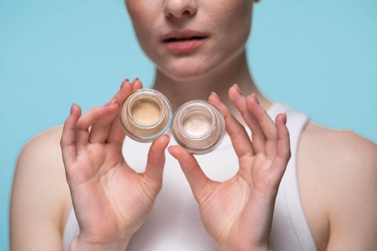La_formula_innovativa_del_Nyx_Bare_With_Me_Concealer_Serum_wuQd948aNz - Confidenze24 Source: Ron Lach - pexels - Close-up of a woman holding skincare jars against a blue background, showcasing beauty and self-care.