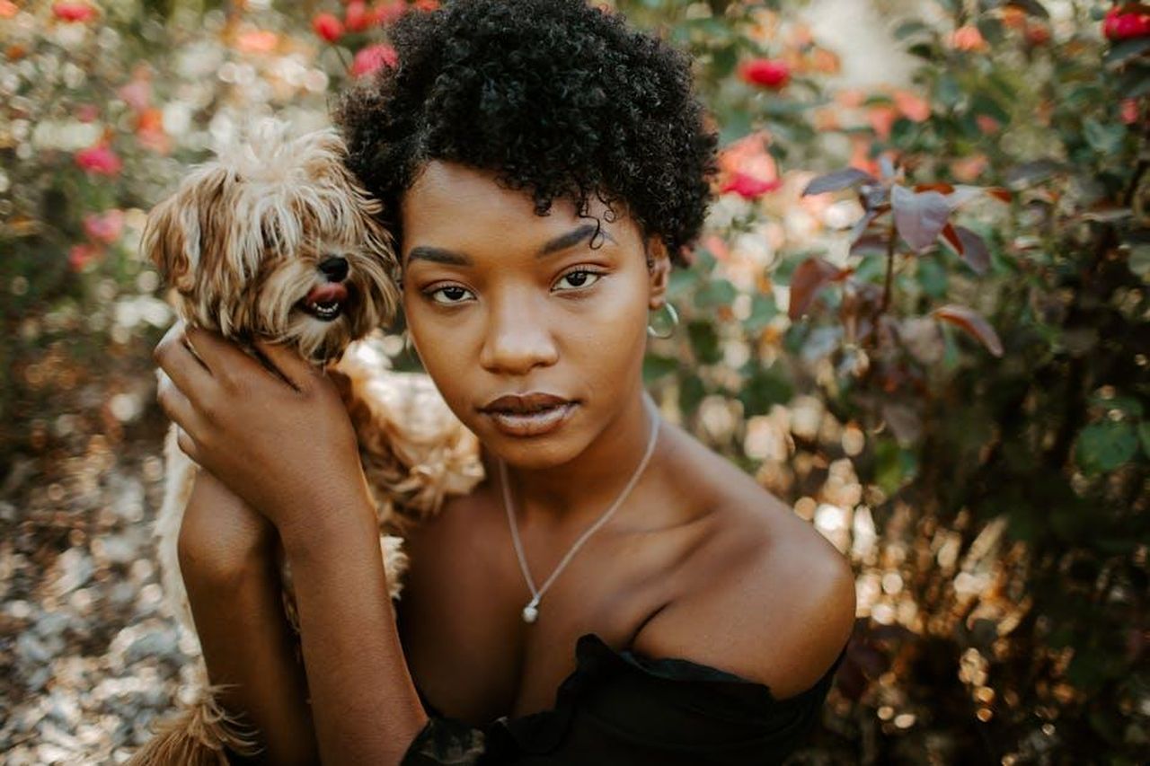 La_gestione_responsabile__la_chiave_avn05NVWTC - Confidenze24 Source: Leah Newhouse - pexels - An African American woman with a small dog in a flower-filled garden, radiating natural beauty.