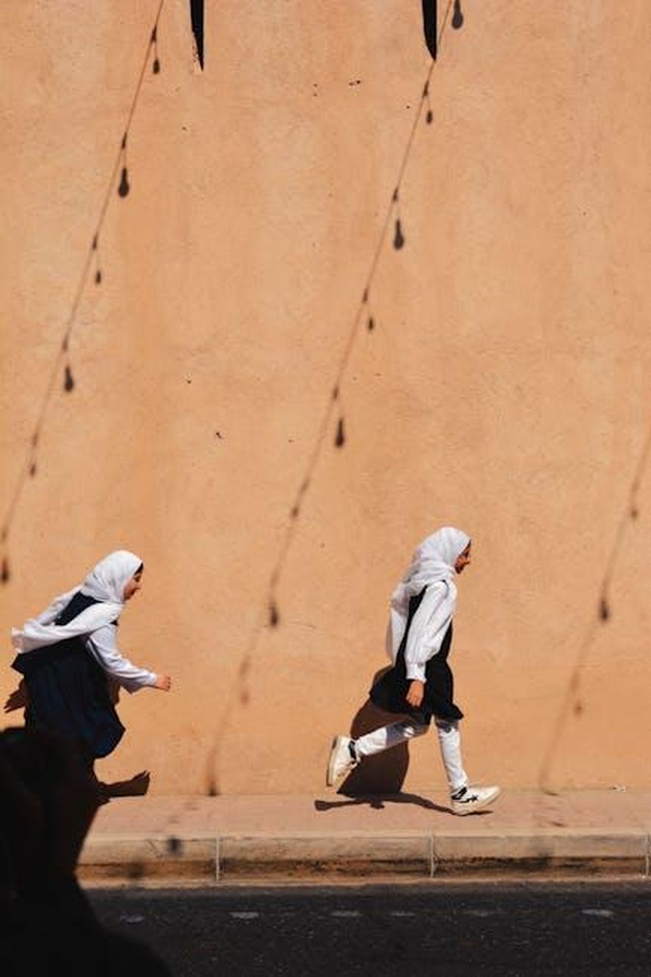 La_giovinezza_e_leducazione_di_Tina_Louise_CAatoX2SPh - Confidenze24 Source: Reyyan - pexels - Two young girls run energetically past a sun-dappled wall in Oman, capturing a moment of joyful childhood.