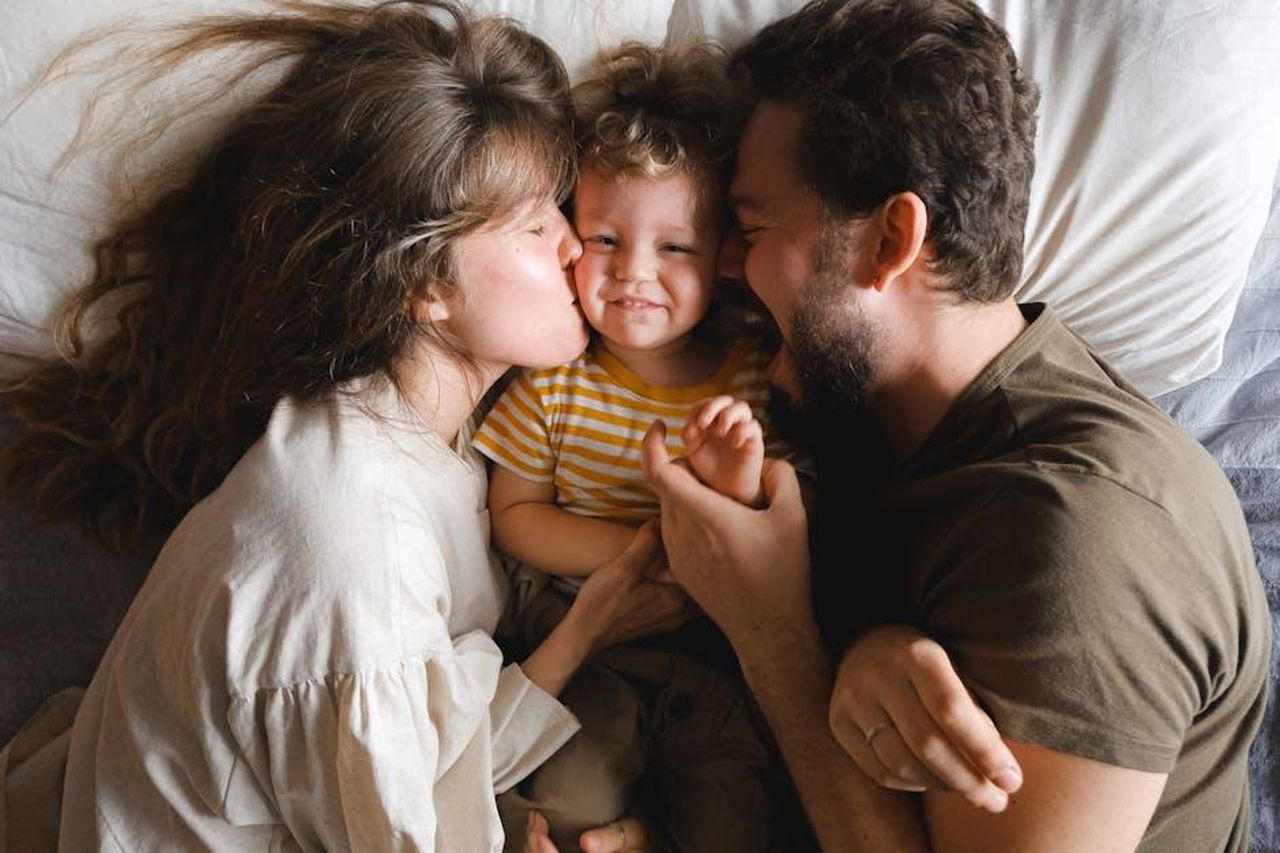 La_loro_esperienza_condivisa_come_padri_BQSNROdTZU - Confidenze24 Source: Anna Shvets - pexels - A joyful family lying together on a bed, showcasing love and happiness.