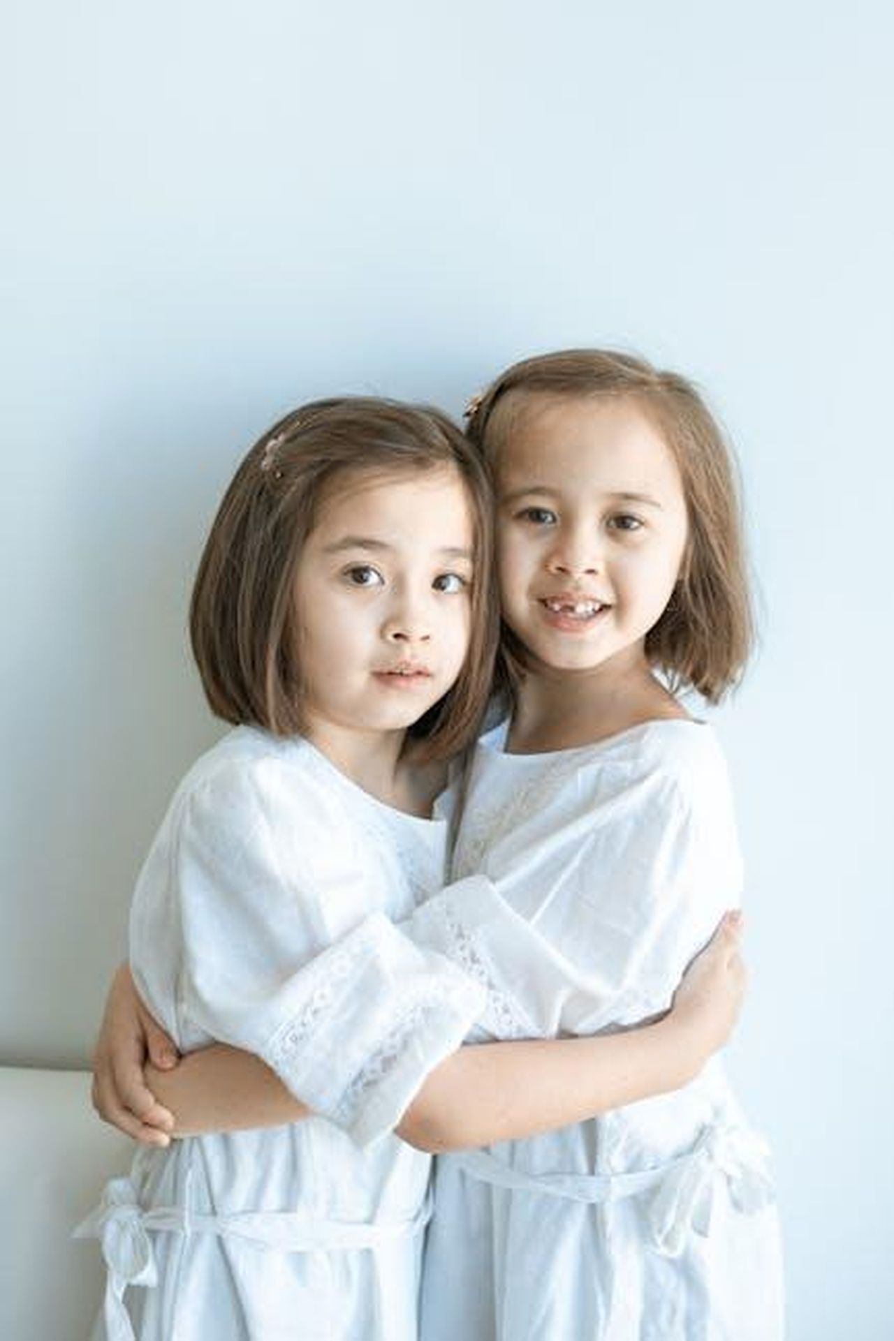 La_percezione_del_pubblico_e_le_critiche_sui_nepobabies_lhqrB13vba - Confidenze24 Source: RDNE Stock project - pexels - Adorable twin sisters embracing, wearing white dresses in a minimalist indoor setting.