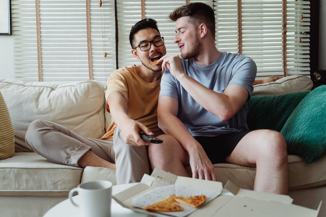 La_pizza_finale_una_collaborazione_speciale_iXTy5URrOy - Confidenze24 Source: Ketut Subiyanto - pexels - A joyful gay couple shares pizza on a cozy sofa, enjoying their time together.