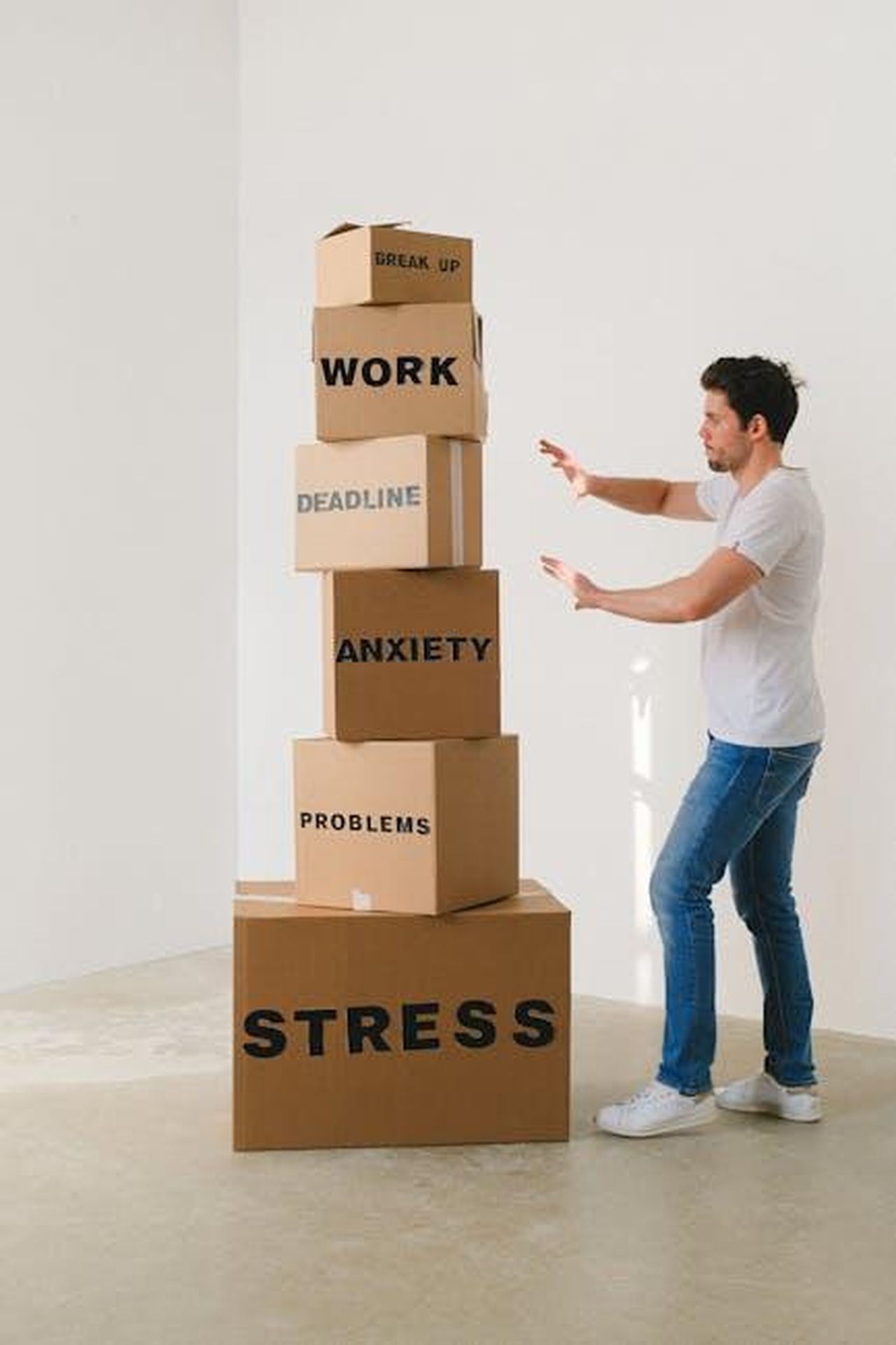 La_pressione_emotiva_e_la_decisione_di_Maria_Vittoria_JcnOPUYYzU - Confidenze24 Source: SHVETS production - pexels - A man in casual attire balances boxes labeled with stress-related words indoors.