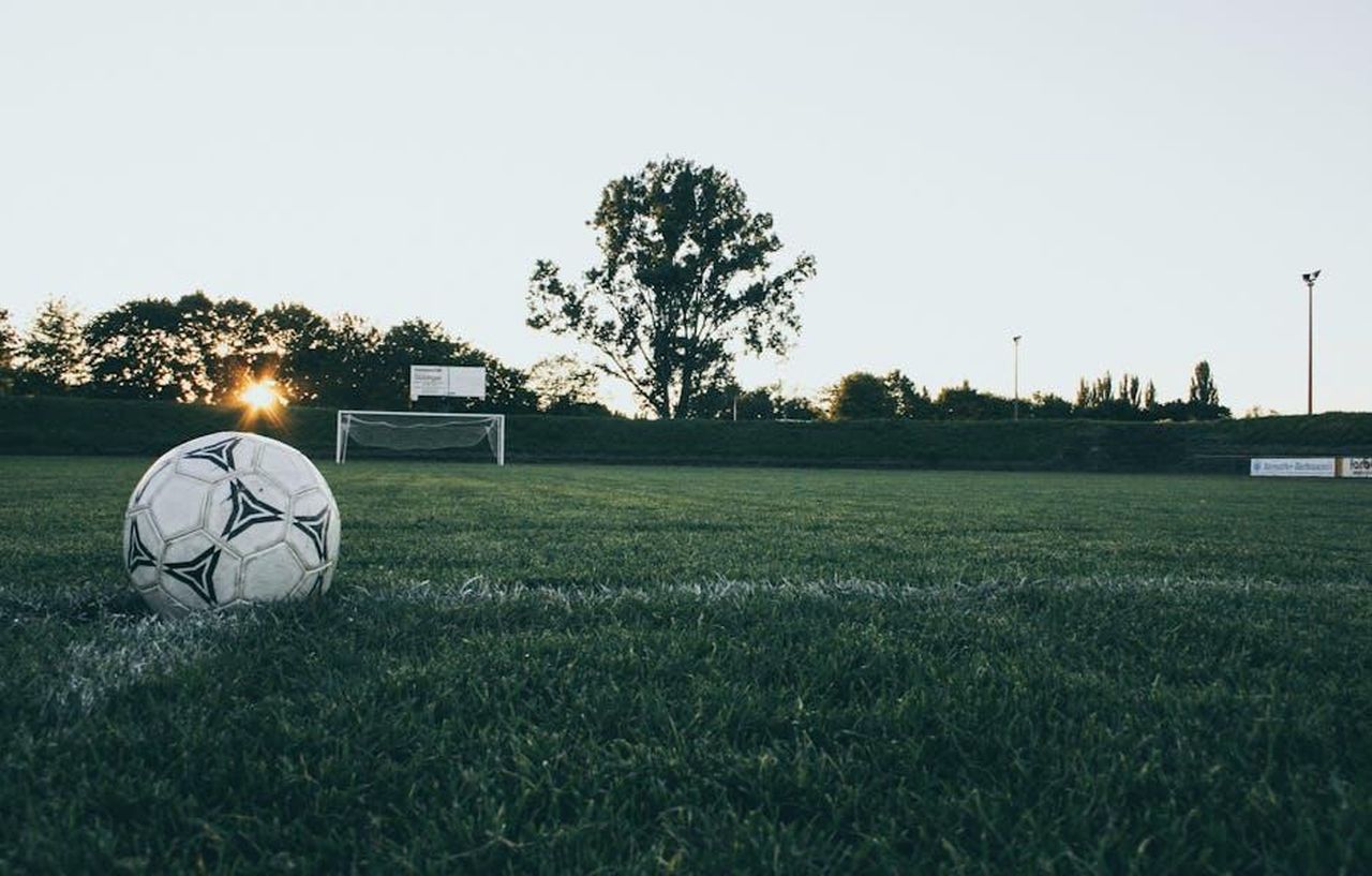La_replica_dellattaccante_8vhEIPqp7u - Confidenze24 Source: Markus Spiske - pexels - Soccer ball on field at sunrise, serene landscape with goalpost in background.