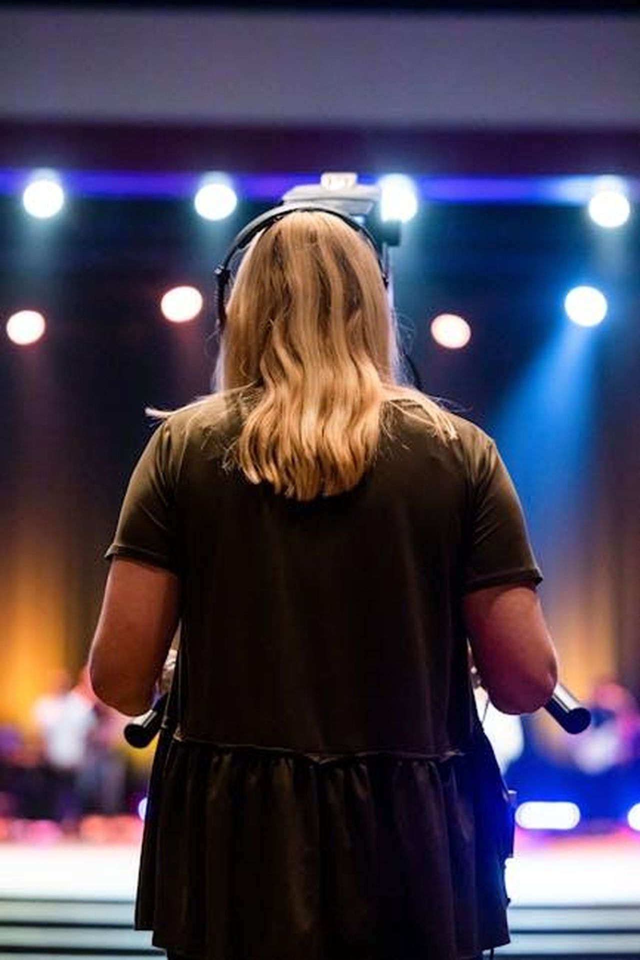 La_responsabilit_della_produzione_del_Grande_Fratello_ajPnul4fon - Confidenze24 Source: Caleb Oquendo - pexels - A female videographer with headphones captures an event indoors, focused on a stage.