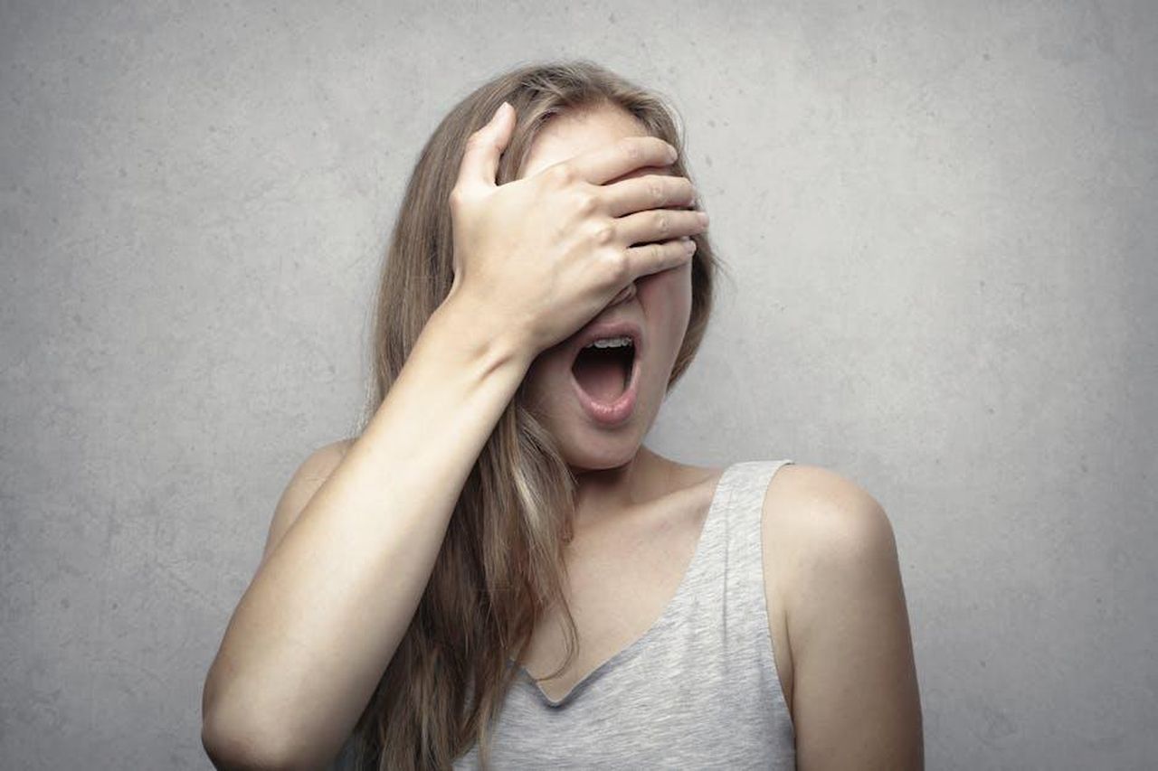 La_rivelazione_di_Giulia_bxO4xB8W8B - Confidenze24 Source: Andrea Piacquadio - pexels - A surprised woman covers her face with one hand, expressing shock and amazement against a gray background.