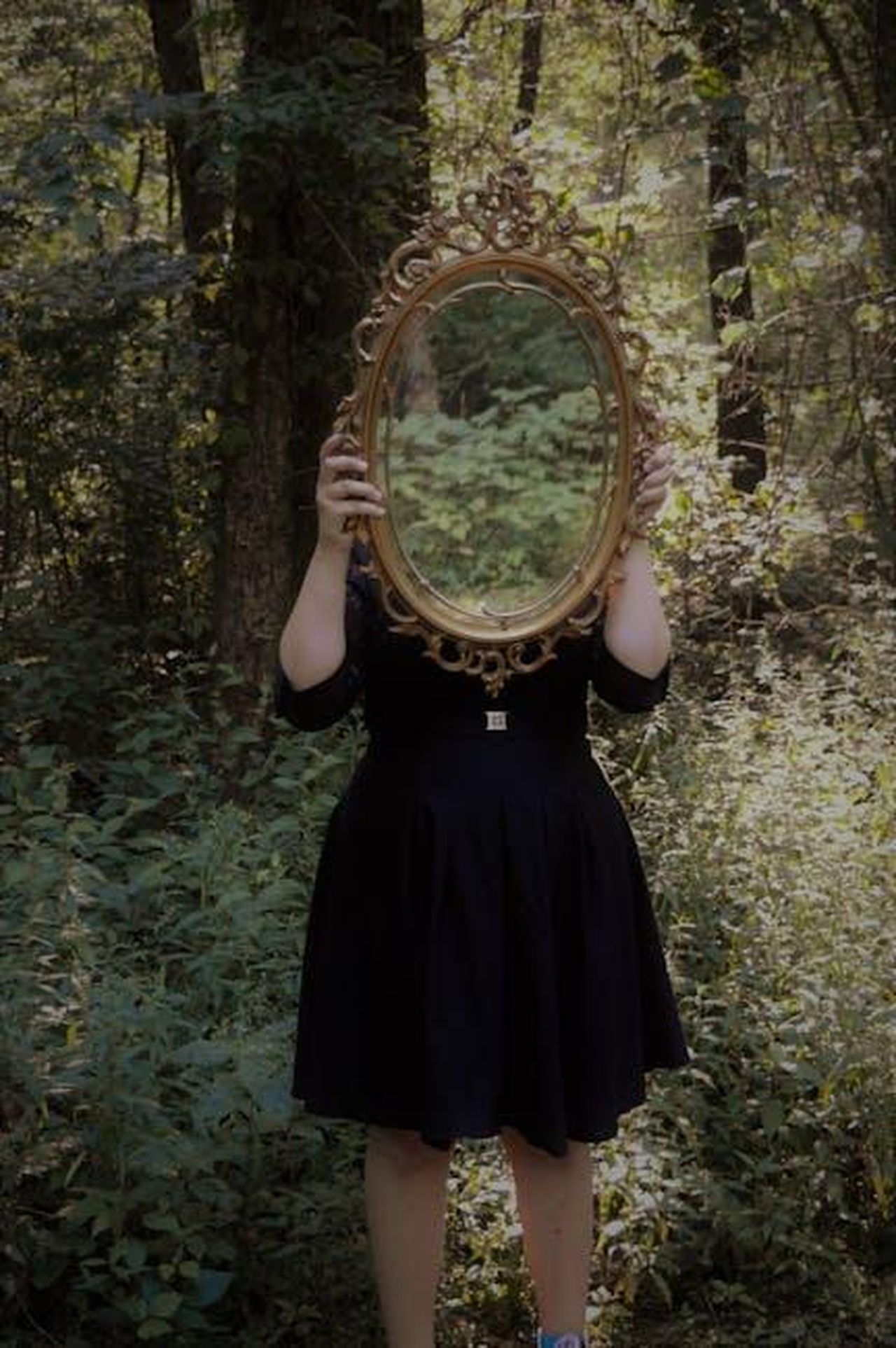 La_scoperta_del_segreto_8YHZBVAhkS - Confidenze24 Source: Tasha Kamrowski - pexels - A woman holds an ornate mirror in a forest setting, reflecting nature.