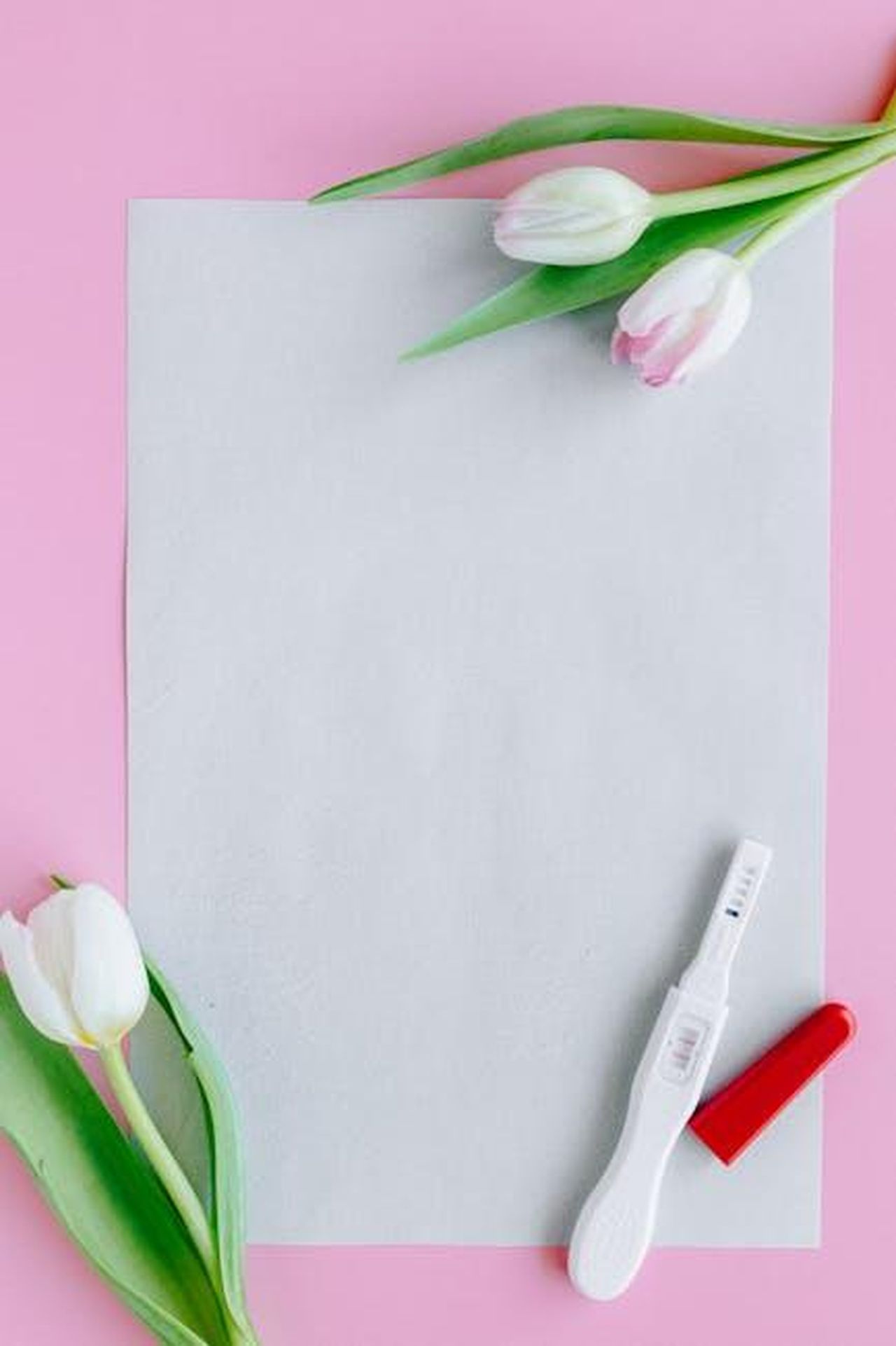 Lannuncio_ufficiale_della_nascita_lJmi8gxErS - Confidenze24 Source: Nataliya Vaitkevich - pexels - Flat lay mockup featuring tulips, blank paper, and pregnancy test on a pink background.