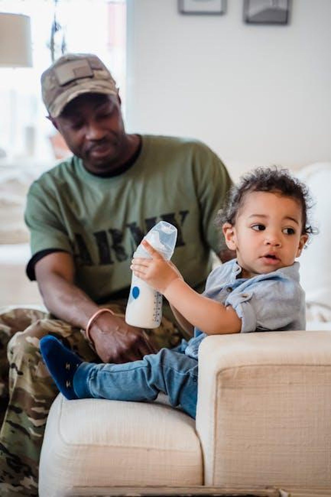 Lartista_ha_confessato_che_lamore_dei_suoi_figli__stato_di_grande_aiuto_skvu3l7pCb - Confidenze24 Source: George Pak - pexels - A father in army uniform sits with his child in a cozy home setting. Family bonding captured.
