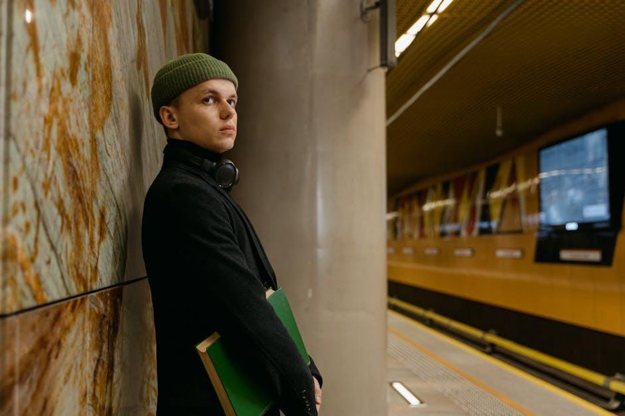 Lattesa_del_pubblico_per_il_confronto_tra_Alfonso_e_gli_altri_concorrenti_33nWXAN96U - Confidenze24 Source: MART PRODUCTION - pexels - Man in a green hat waiting at a subway station with a book in hand.