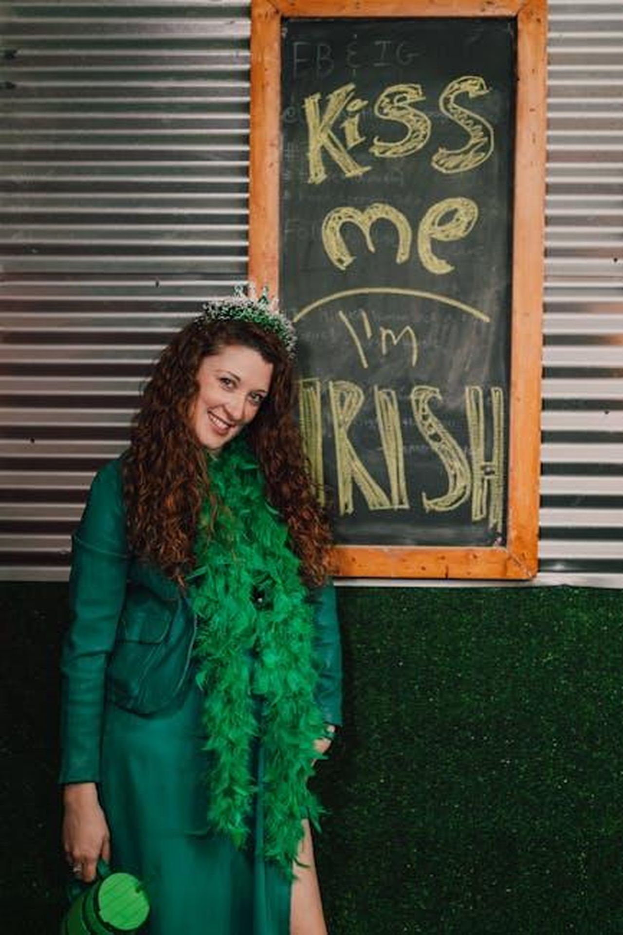 Le_dichiarazioni_di_Ashley_St_Clair_IxOnZiSOKf - Confidenze24 Source: RDNE Stock project - pexels - Smiling woman in green outfit posing by Irish-themed blackboard.
