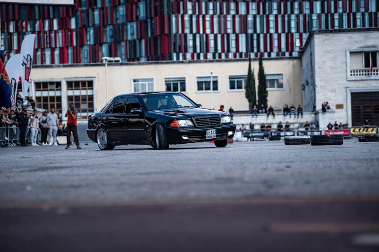 Le_dinamiche_interne_della_casa_vRf3wyYHcx - Confidenze24 Source: Ardit Mbrati - pexels - A sleek black car performs in an urban environment with an audience observing.