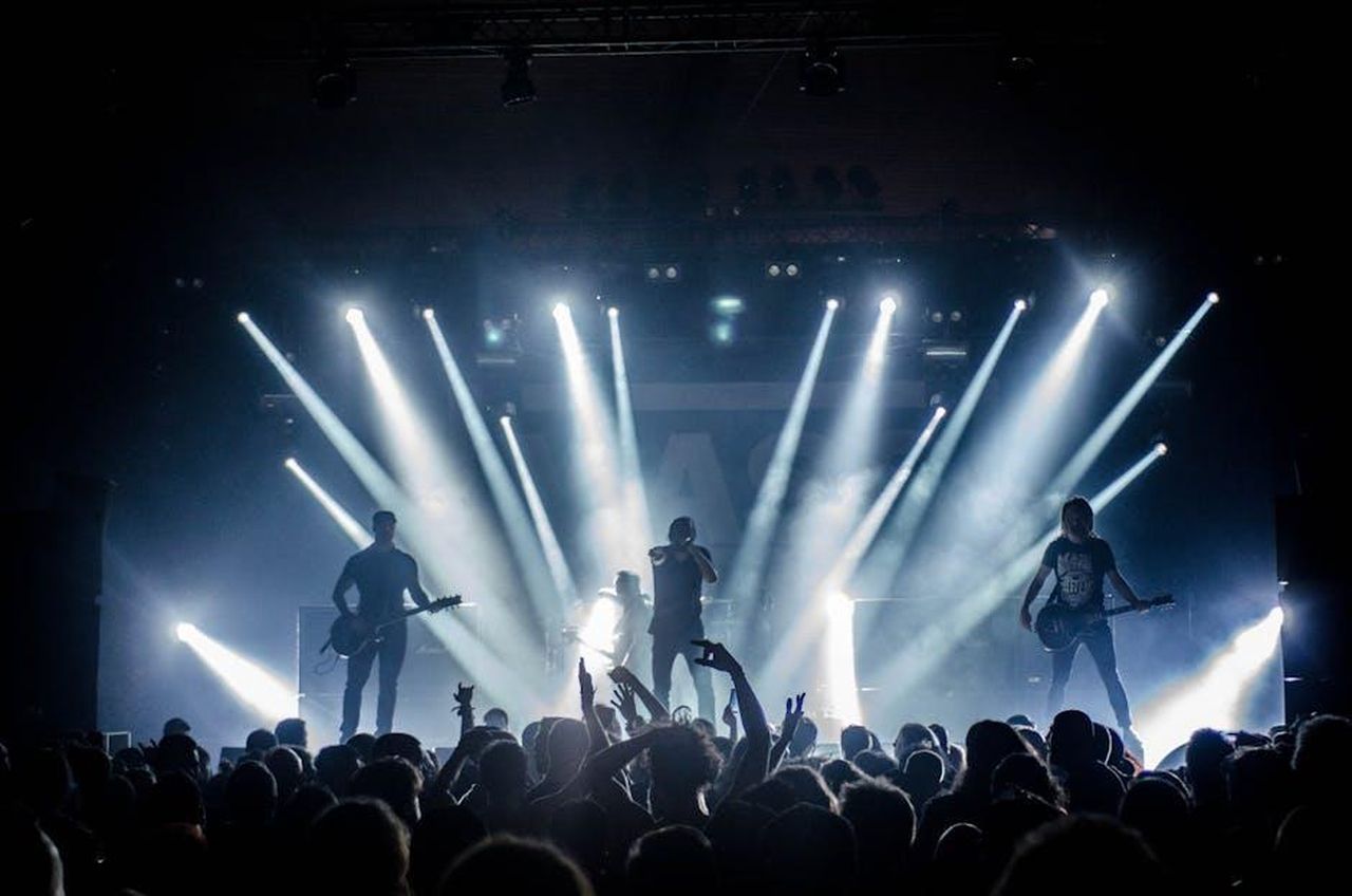 Le_dinamiche_interpersonali_nella_casa_del_Grande_Fratello_NxCXH2ZYzZ - Confidenze24 Source: Thibault Trillet - pexels - Energetic live concert with musicians performing on stage, engaging the crowd with vibrant lighting effects.