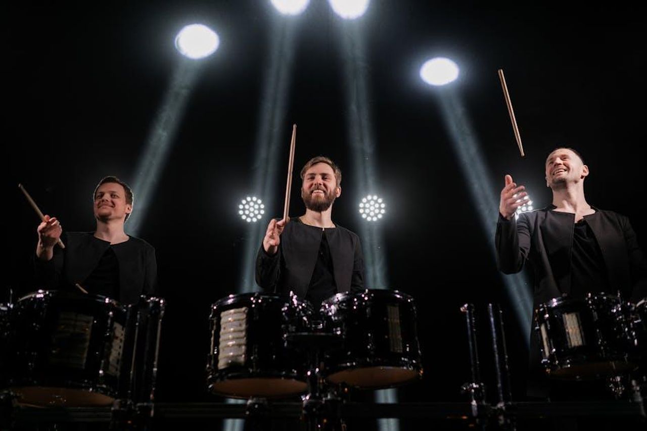Le_frecciatine_di_Stefania_yA3HHe43dk - Confidenze24 Source: Alena Darmel - pexels - Three male drummers performing with drumsticks under vibrant stage lights.