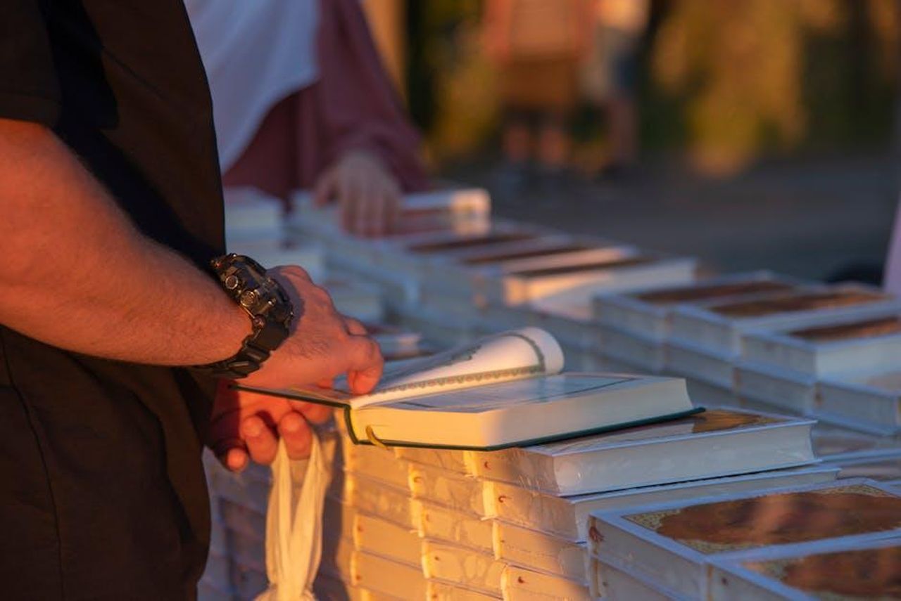 Le_otto_sezioni_del_Salone_unmooNK7Fw - Confidenze24 Source: Xhemi Photo - pexels - A person flipping through books at an outdoor market stall during sunset.