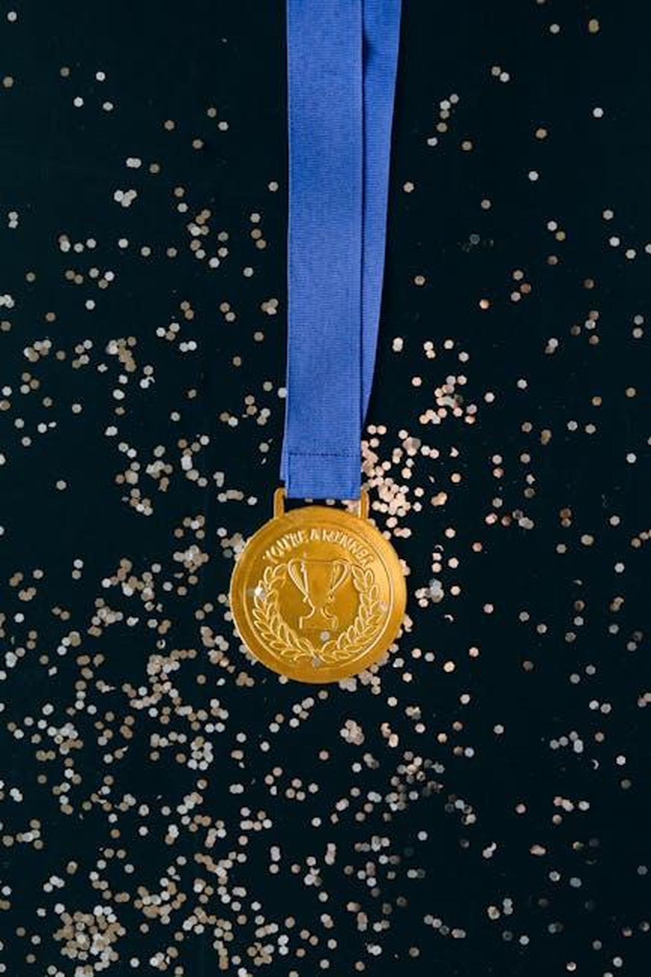 Le_possibilit_di_vittoria_di_Lorenzo_PAiehxFY3Y - Confidenze24 Source: Nataliya Vaitkevich - pexels - Close-up of a shimmering gold medal with blue ribbon on a black surface, symbolizing victory and achievement.