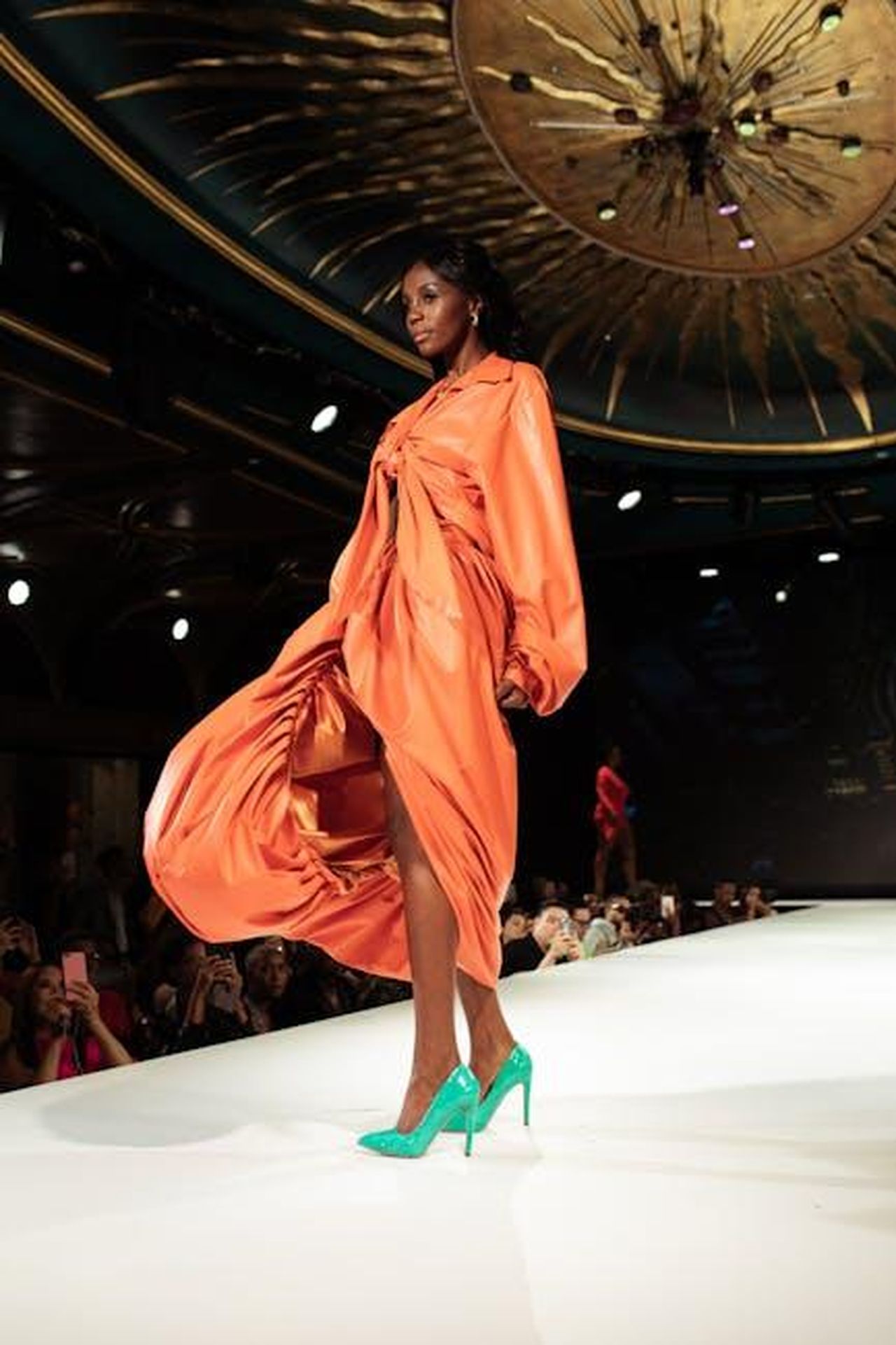 Le_reazioni_del_pubblico_e_le_dinamiche_della_casa_e57JLk4cMj - Confidenze24 Source: nappy - pexels - An African American model struts confidently in an orange dress during a fashion show.