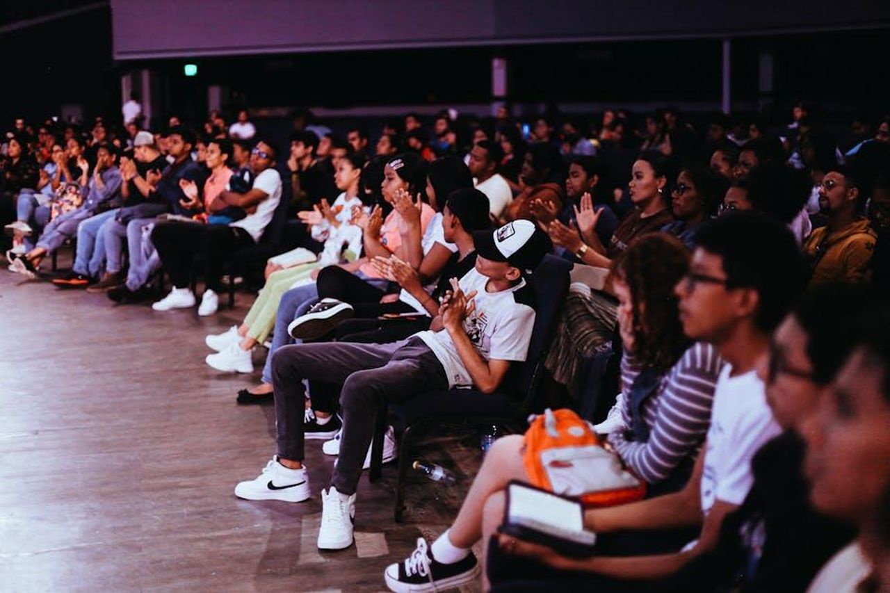 Le_reazioni_del_pubblico_sui_social_media_aWsZtyC5aT - Confidenze24 Source: Alejandra Montenegro - pexels - A diverse crowd seated in an auditorium applauds a live performance.