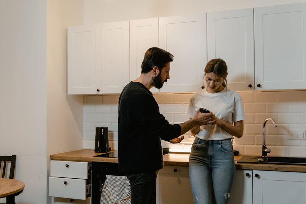 Le_sfide_dellamore_la_pressione_familiare_IXOHBsQJQs - Confidenze24 Source: MART PRODUCTION - pexels - A young couple engages in a tense discussion in a modern kitchen setting.