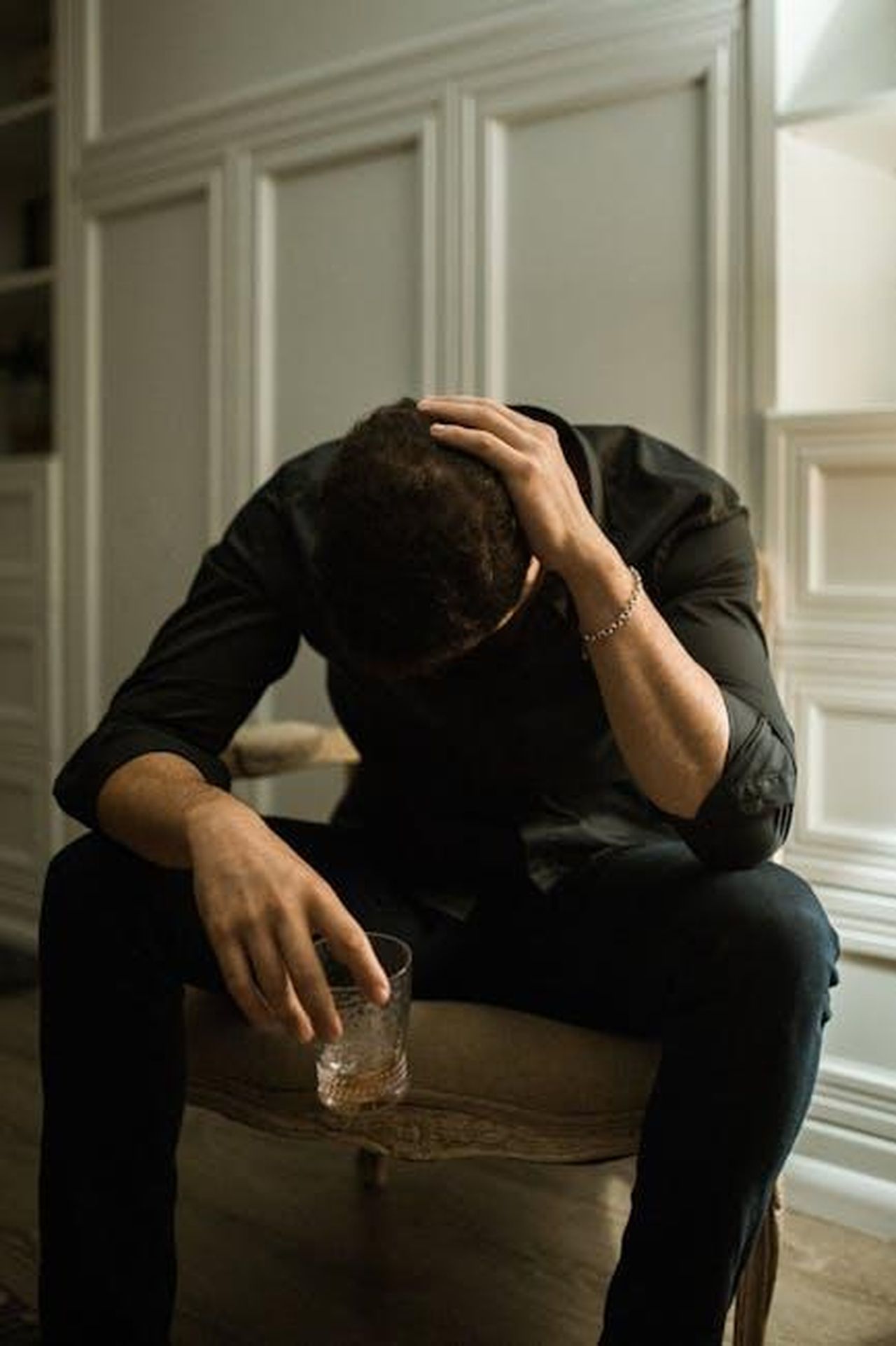 Le_sfide_di_Wallen_e_il_suo_passato_RCf8hsZmTv - Confidenze24 Source: RDNE Stock project - pexels - Man in distress seated indoors, head in hand, holding a drink, reflecting solitude.