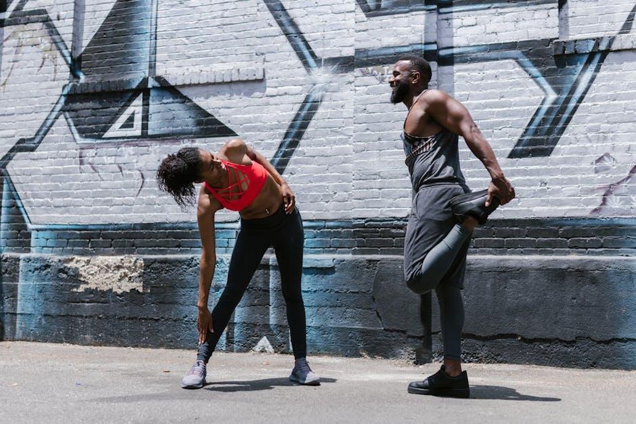 Leone_23_luglio__22_agosto_EgX6CHUiYW - Confidenze24 Source: RDNE Stock project - pexels - Two adults stretching against a graffiti wall outdoors, showcasing strength and fitness.