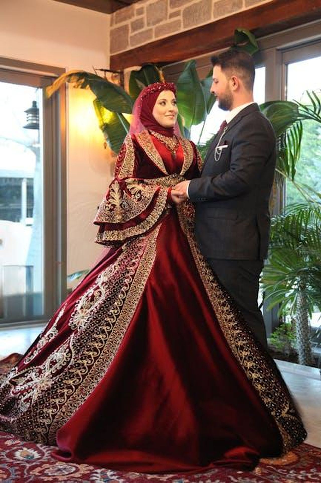 Leslie_Anne_Hackman_WCQO74oL6y - Confidenze24 Source: Dilara Doğar - pexels - Couple in exquisite traditional wedding attire posing indoors with lush greenery.