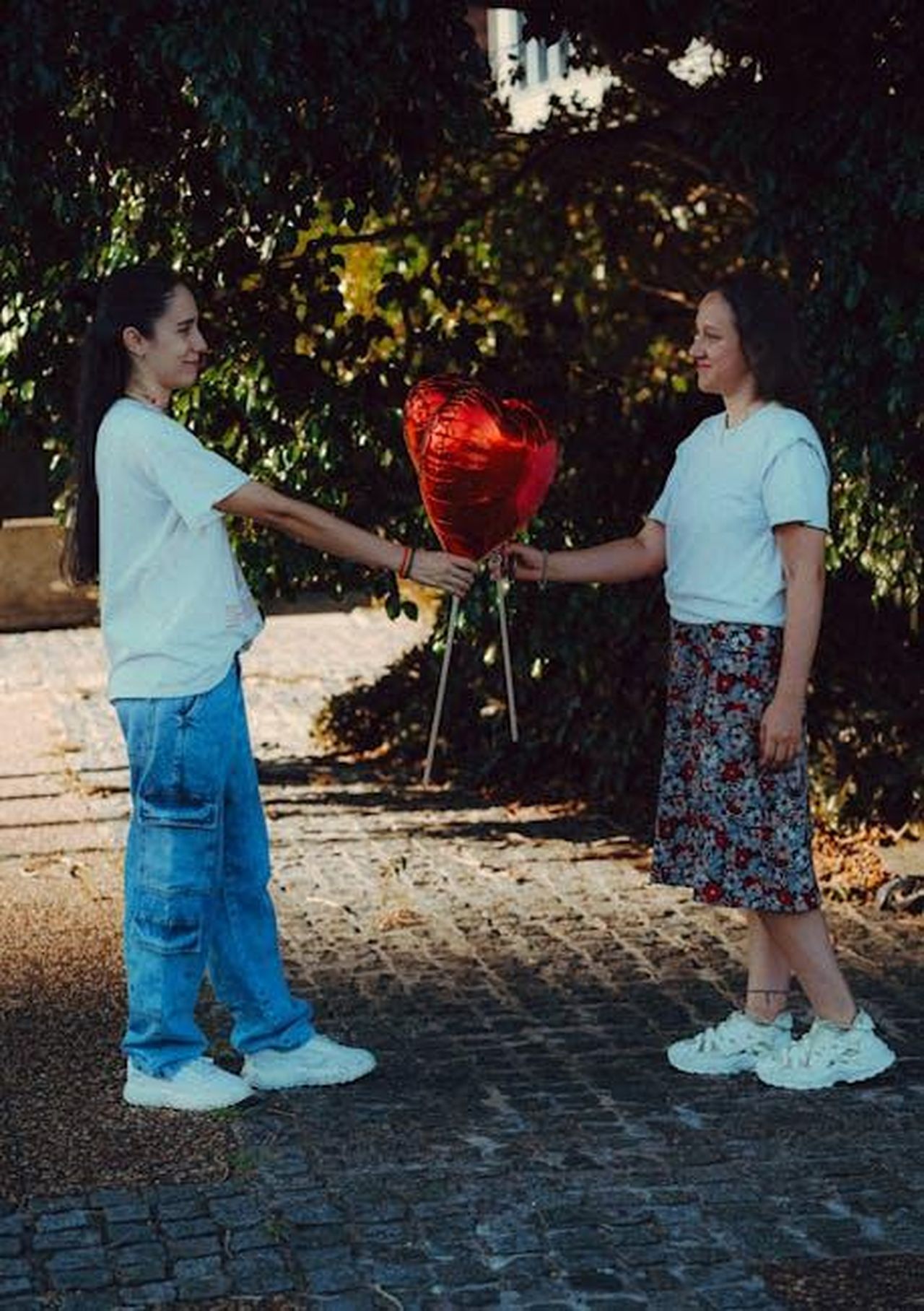 Limportanza_del_supporto_di_Kyle_Richards_7dGJr7dbiE - Confidenze24 Source: Andres Idda Bianchi - pexels - Two women exchange a red heart balloon in an outdoor park setting, symbolizing friendship.
