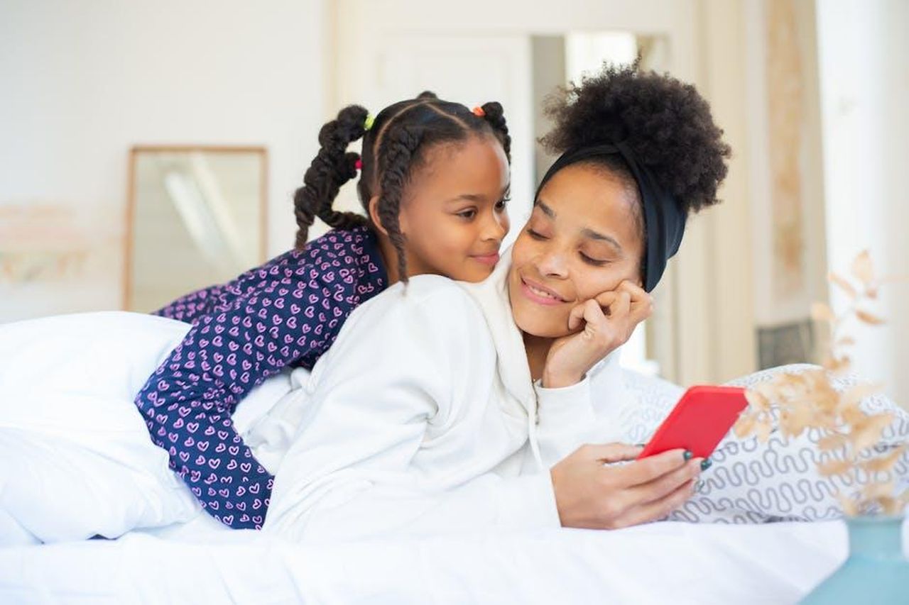 Limportanza_della_comunicazione_nei_momenti_difficili_uzySew70wW - Confidenze24 Source: Kampus Production - pexels - A heartwarming moment between a mother and daughter embracing while using a smartphone indoors.