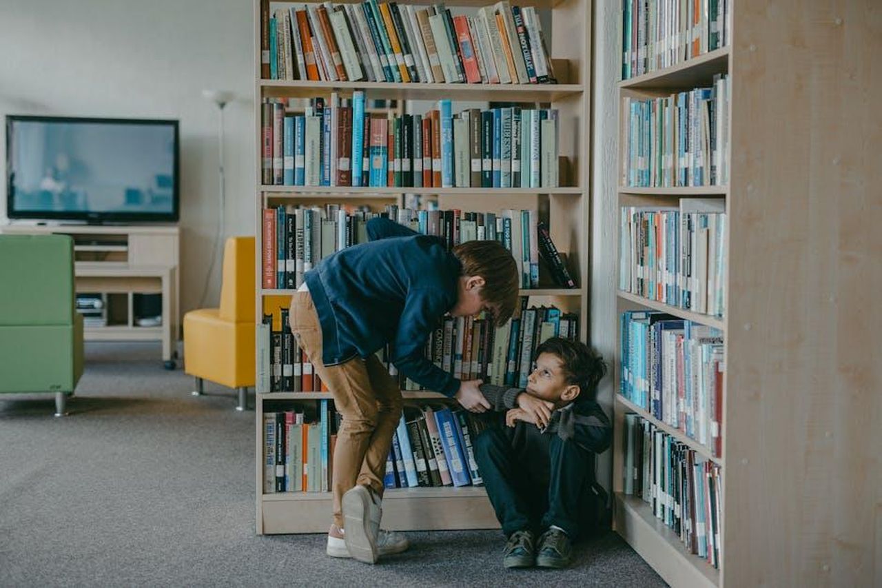 Lintervento_della_maestra_e_la_reazione_delluomo_TXWkRuXvew - Confidenze24 Source: Mikhail Nilov - pexels - A child bullies another student in a school library, highlighting social issues.