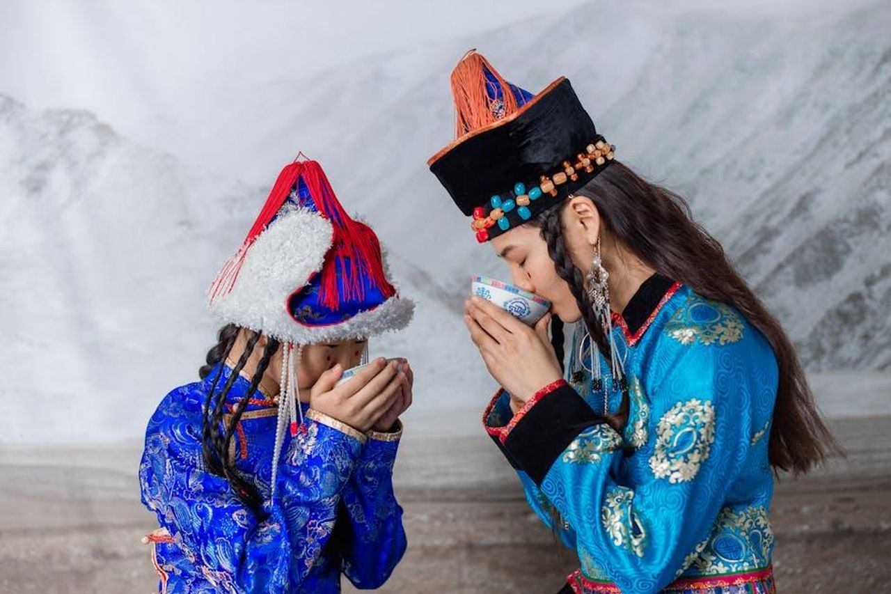 Lorgoglio_di_Amanda_kp7YT1t4v9 - Confidenze24 Source: cottonbro studio - pexels - Two women in vibrant Mongolian clothing sharing a drink, showcasing cultural heritage.