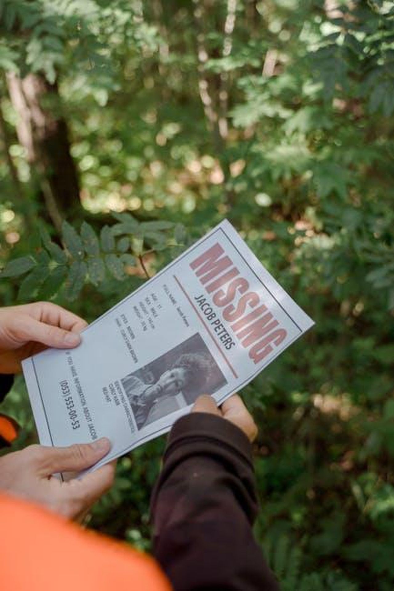 Manuela_sparisce_e_viene_ritrovata_nel_bosco_come_finisce_Un_passo_dal_cielo_8_ncoL3B19Lu - Confidenze24 Source: Ron Lach - pexels - Two hands holding a missing person flyer in a forest setting, implying search or investigation.