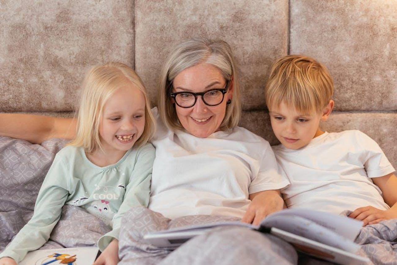 Mariella__affiatata_con_Mimmo_Rossella_trova_conforto_in_Nunzio_4RtWiYdHB9 - Confidenze24 Source: Mikhail Nilov - pexels - Smiling grandmother reading a book with her grandchildren in bed for family bonding time.