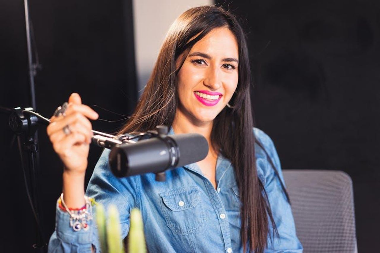 Mark_Wright_condivide_un_importante_annuncio_di_carriera_dopo_lintrusione_7qui1NBiGH - Confidenze24 Source: Los Muertos Crew - pexels - A woman in a denim shirt, smiling while podcasting in a studio with a professional microphone.