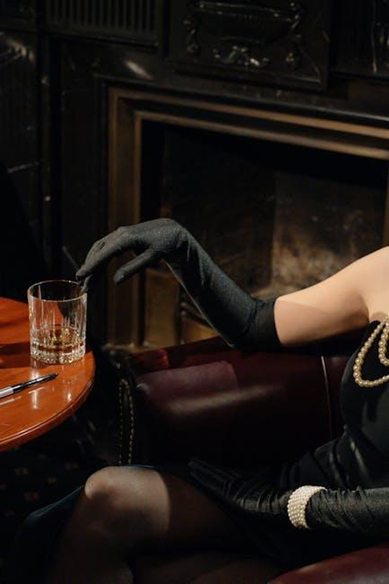 Michelle_Collins_ha_lasciato_il_ruolo_di_Cindy_cGgZZ66Tob - Confidenze24 Source: cottonbro studio - pexels - A sophisticated woman in black gloves and pearls holds a whiskey glass in a vintage setting.